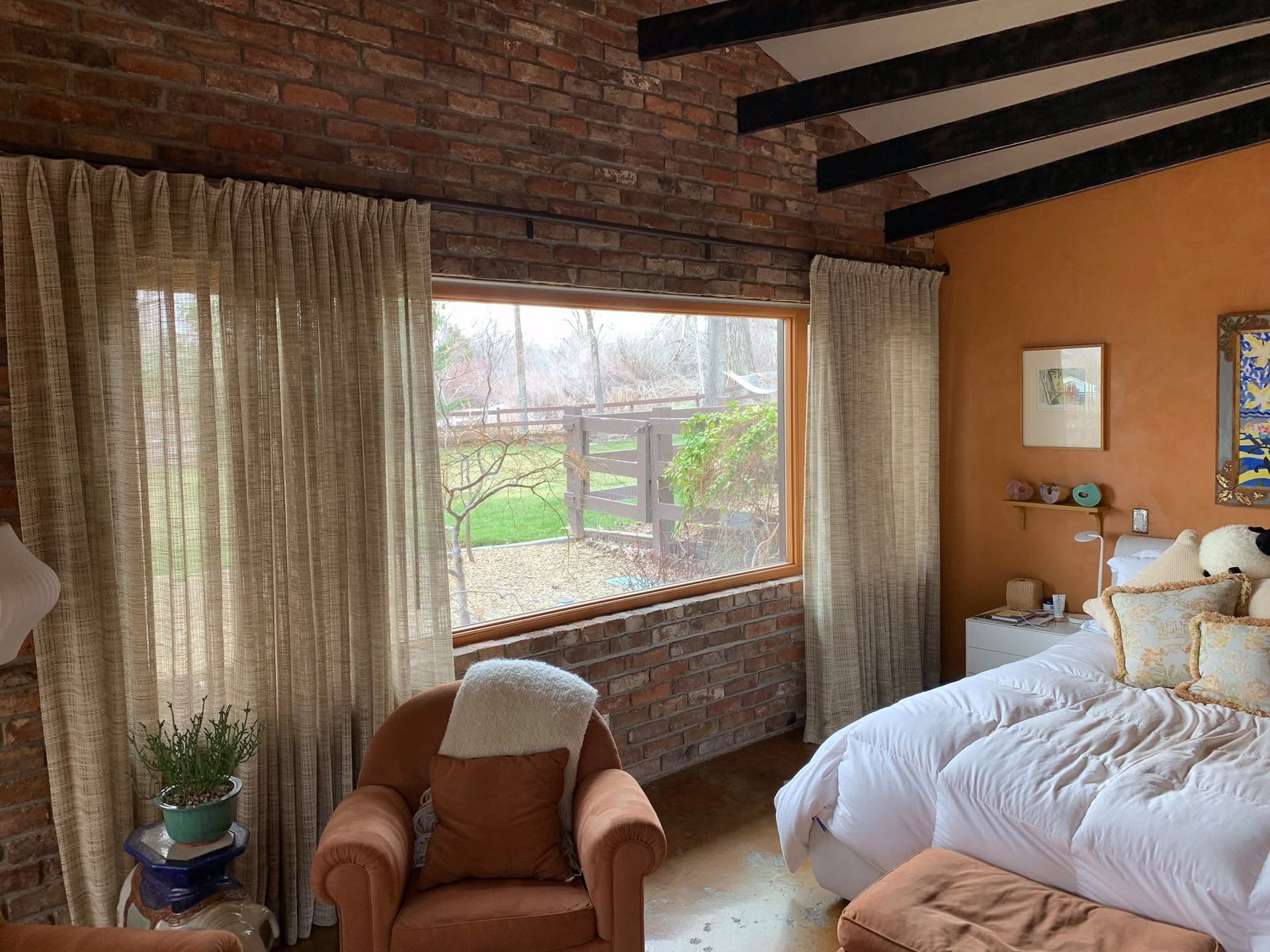 Cozy bedroom with brick walls, large window, tan chair, and a white bedspread