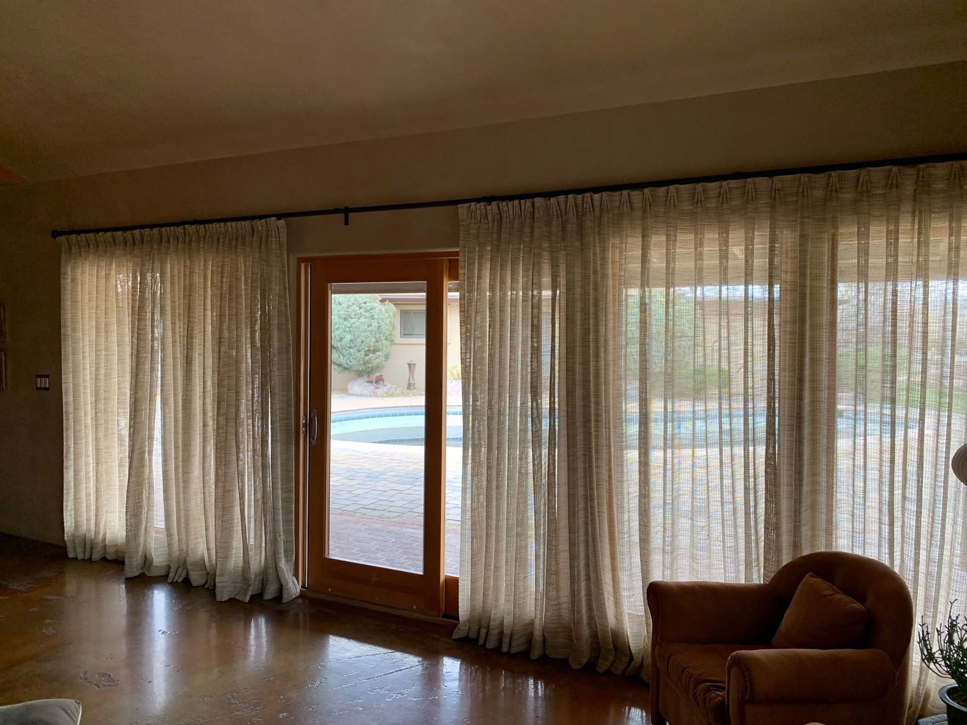 Living room with sheer curtains, a glass door, and a brown armchair by a sunny patio view