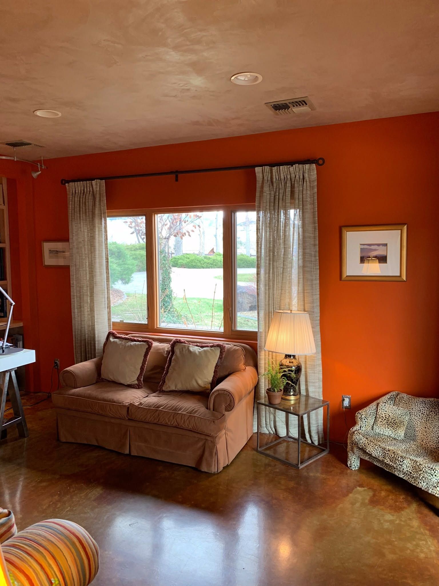 Orange living room with sofa by window, framed art, lamp, and patterned chair on hardwood floor