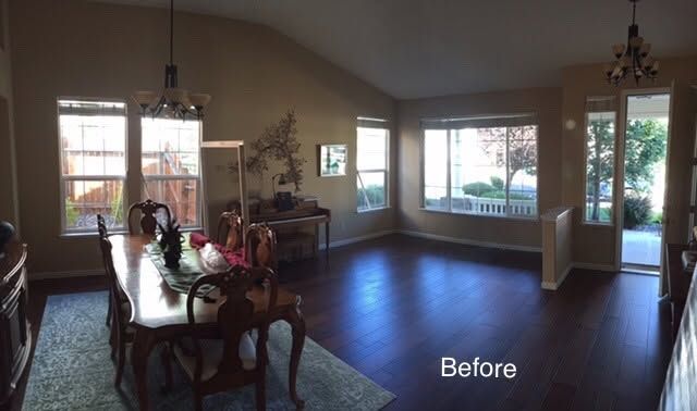 Spacious empty dining and living room with dark floors, large windows, and a dining table by the wall.