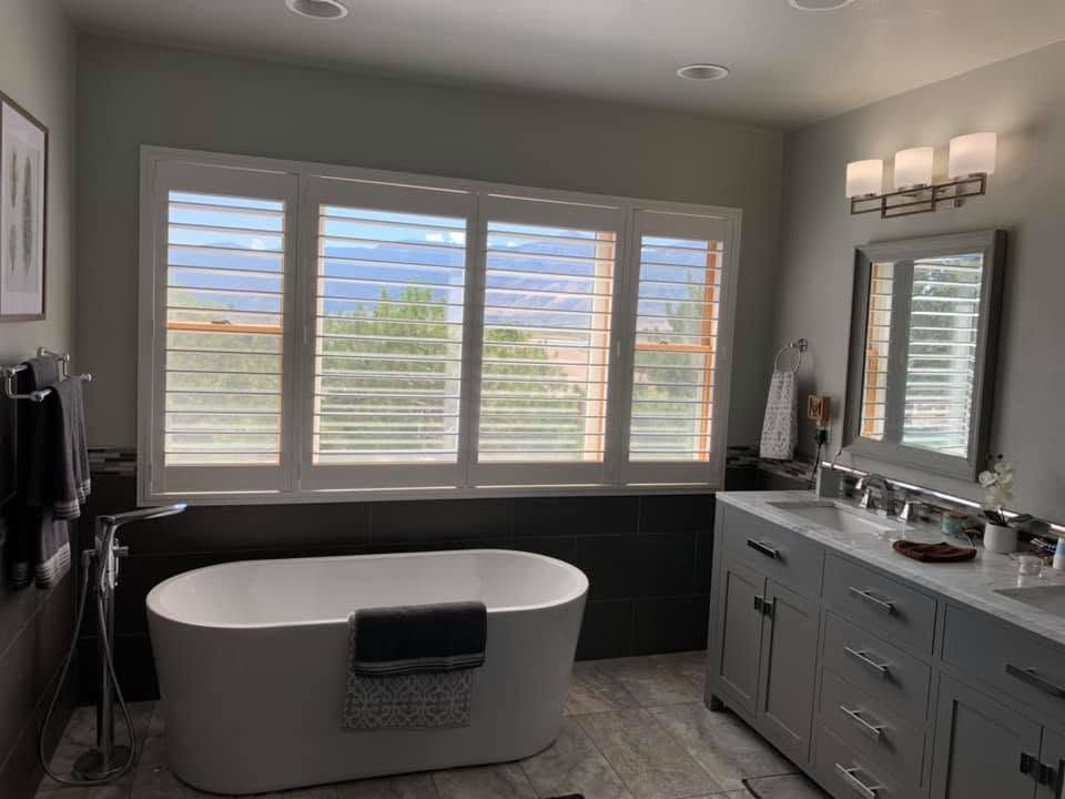 Modern bathroom with a freestanding tub, double vanity, large window, and mirror under wall sconces.