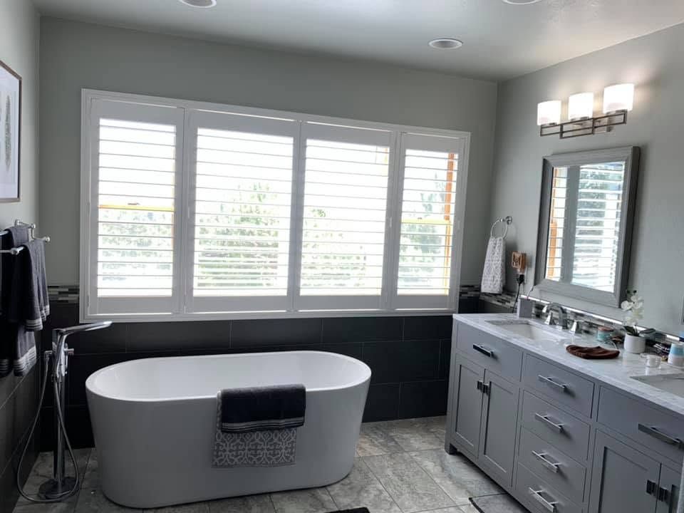 Modern bathroom with a freestanding tub, double vanity, large window, and mirror light fixture