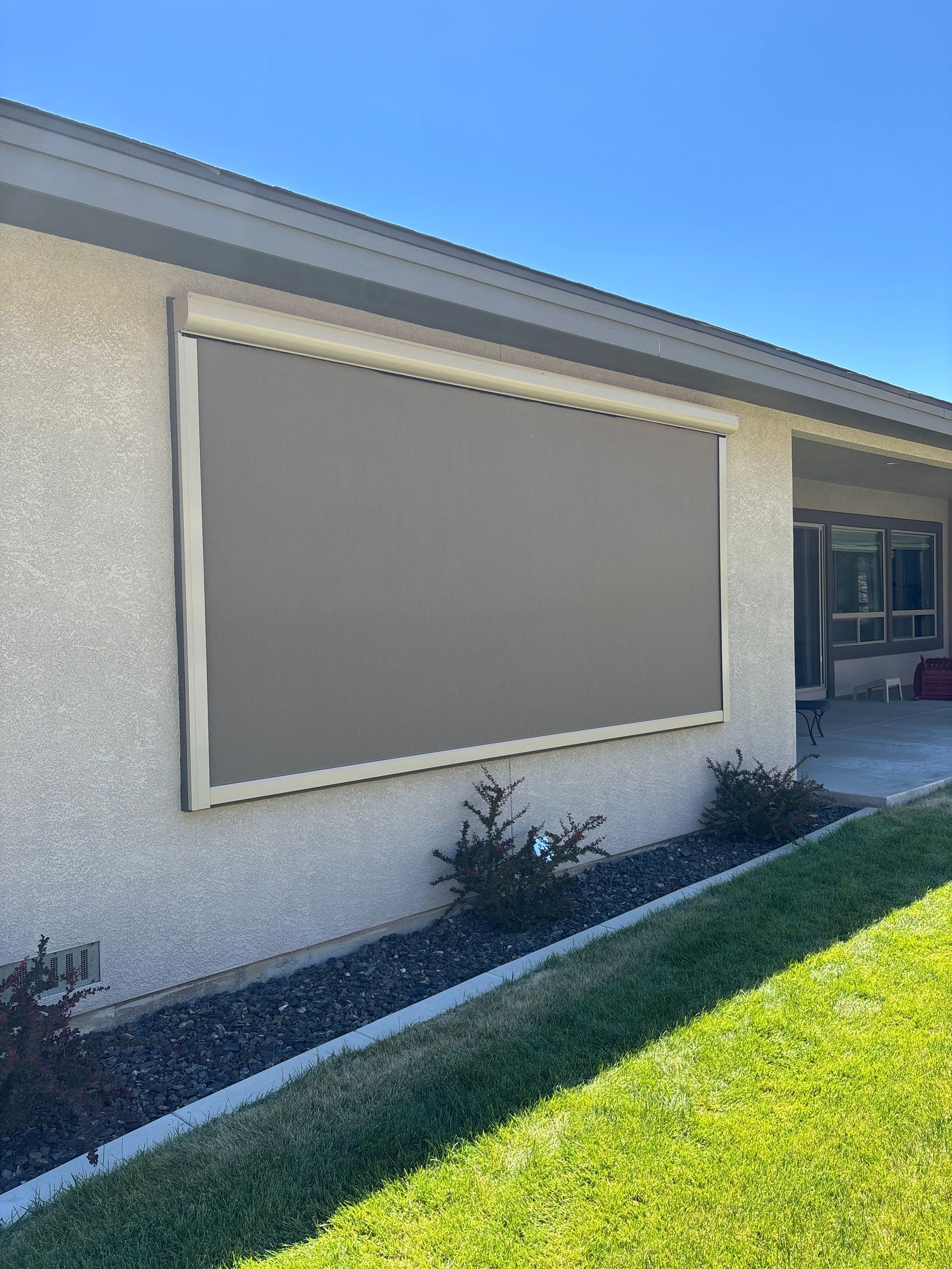 Exterior wall of a house with a large gray window awning above a green lawn and walkway.