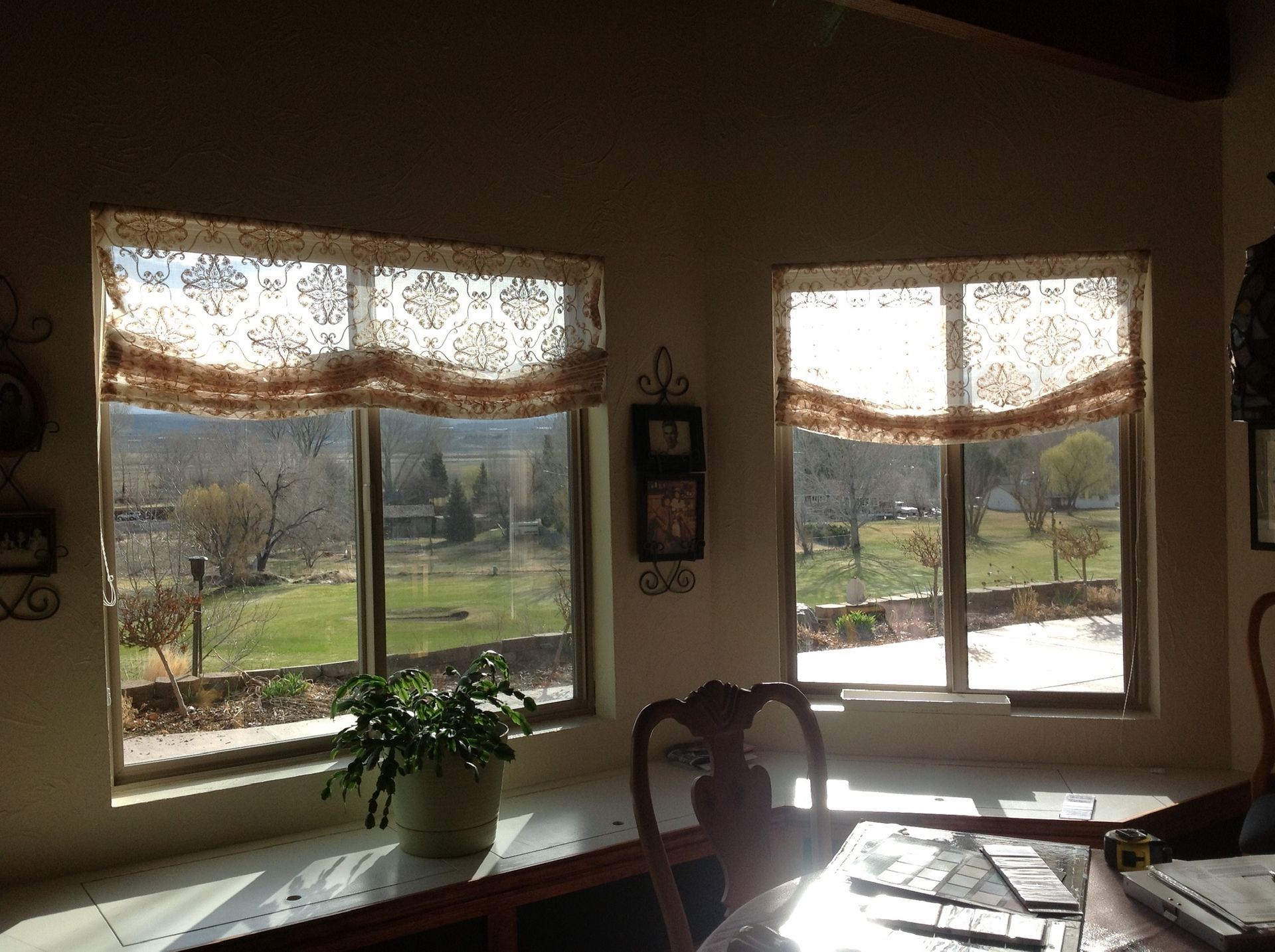 Sunlit kitchen with two windows, a potted plant, and a dining table by a scenic view