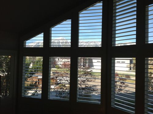 View through white blinds to a sunny suburban neighborhood and blue sky