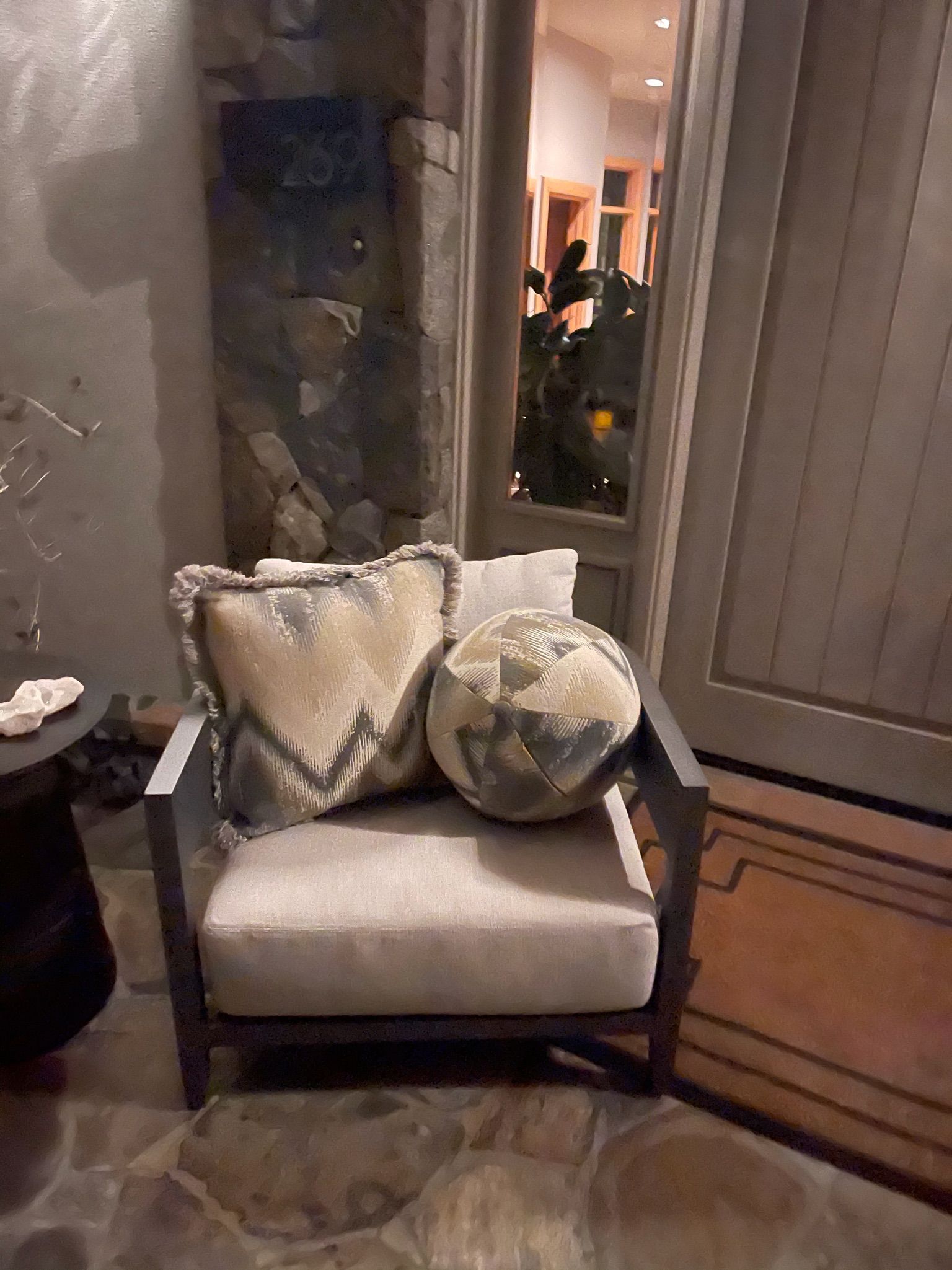 Cozy chair with patterned pillows beside a mirror and door in a warmly lit hallway