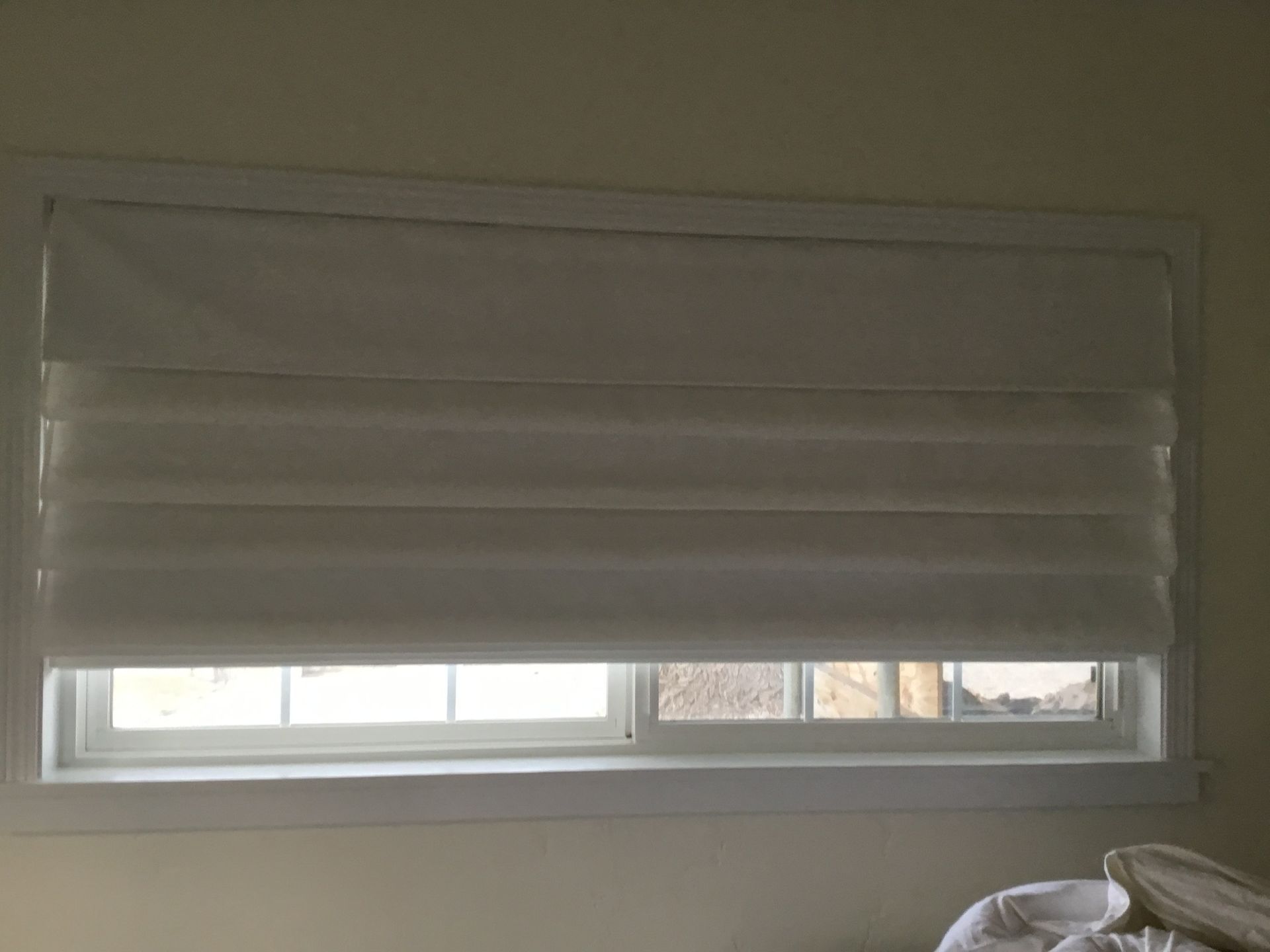 White window blinds partially closed over a small window in a plain room.