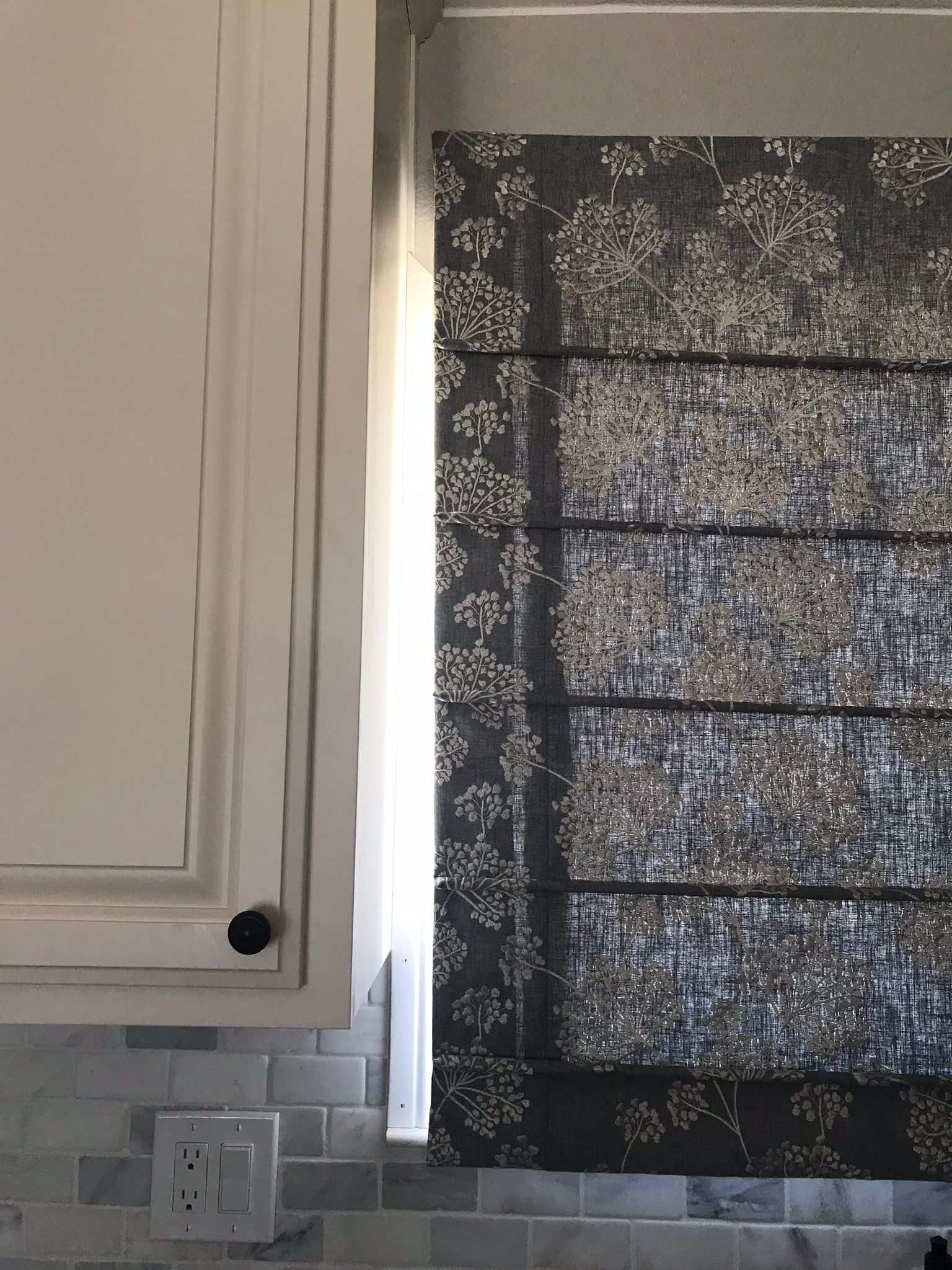 Kitchen cabinet beside a window with a dark patterned curtain and white tile backsplash