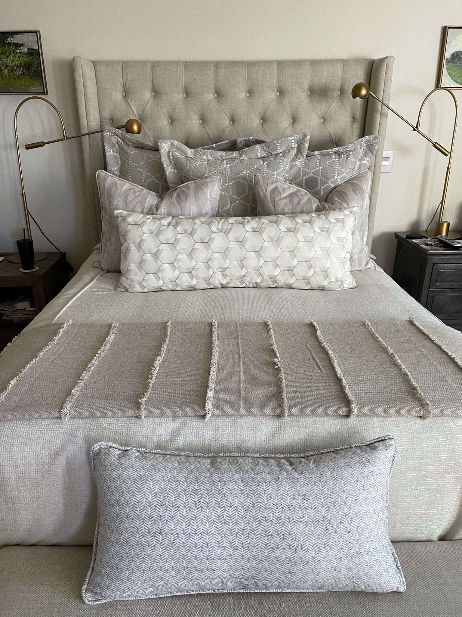 Neatly made bed with silver-gray tufted bedding, pillows, and upholstered headboard in a modern bedroom.