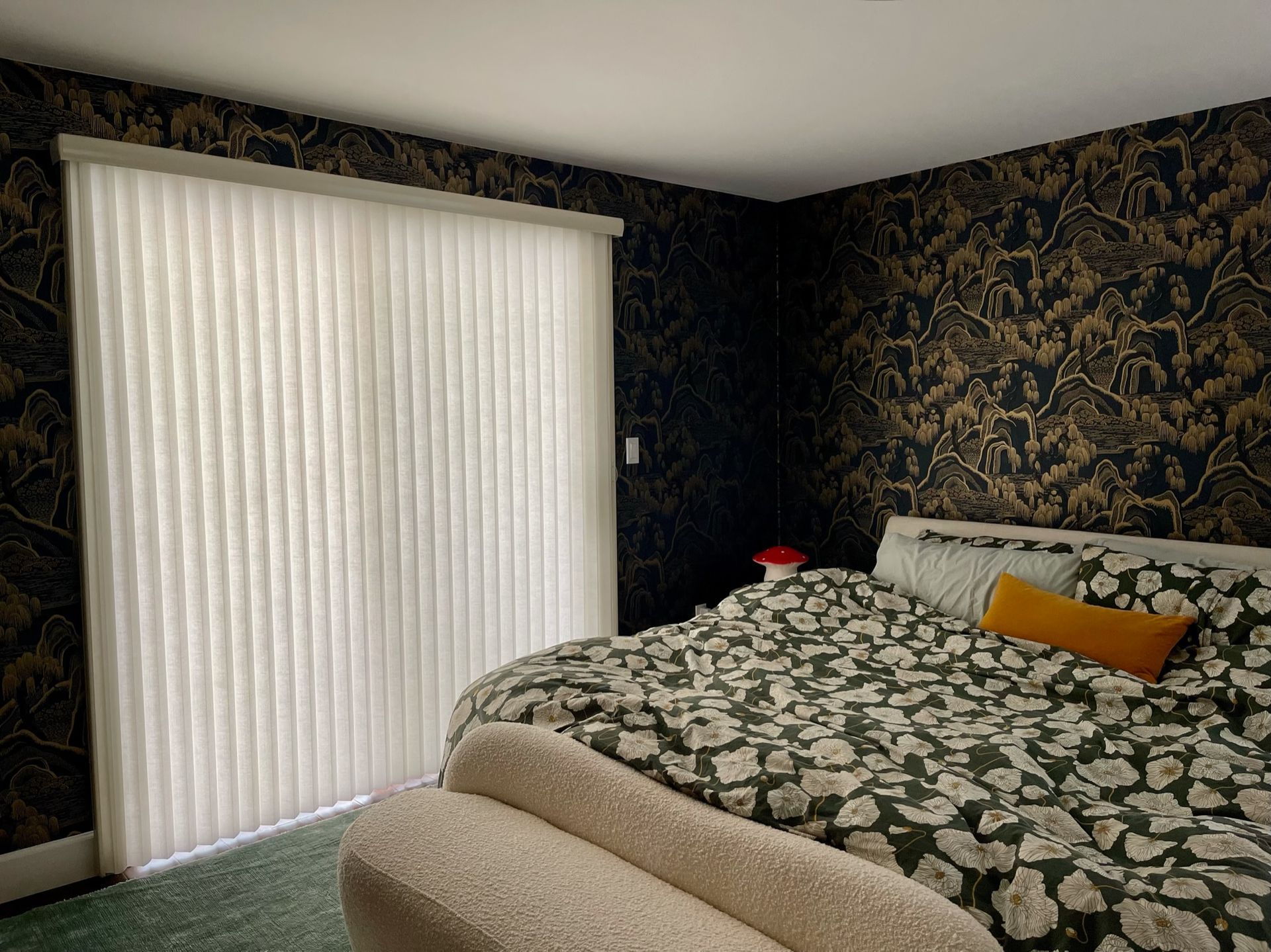 Bedroom with floral wallpaper, beige bedspread, and a large window covered by white vertical blinds