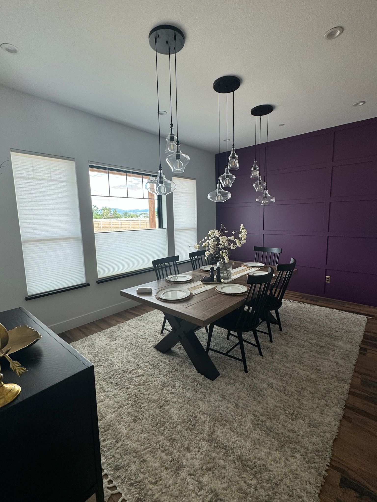 Modern dining room with dark wood table, black chairs, purple accent wall, and large windows.
