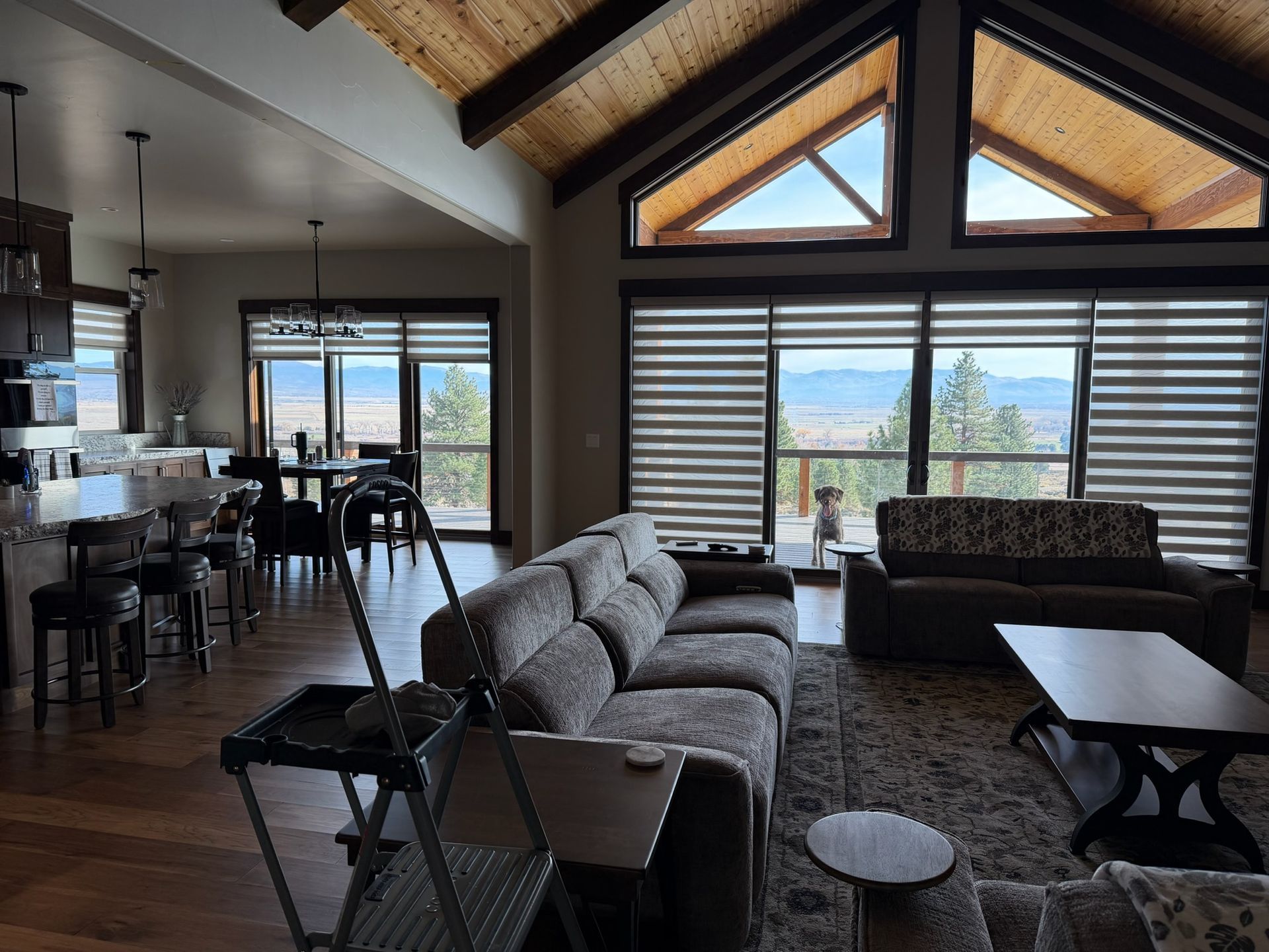 Modern living room with vaulted wood ceiling, gray sofas, and large windows overlooking a lake and mountains