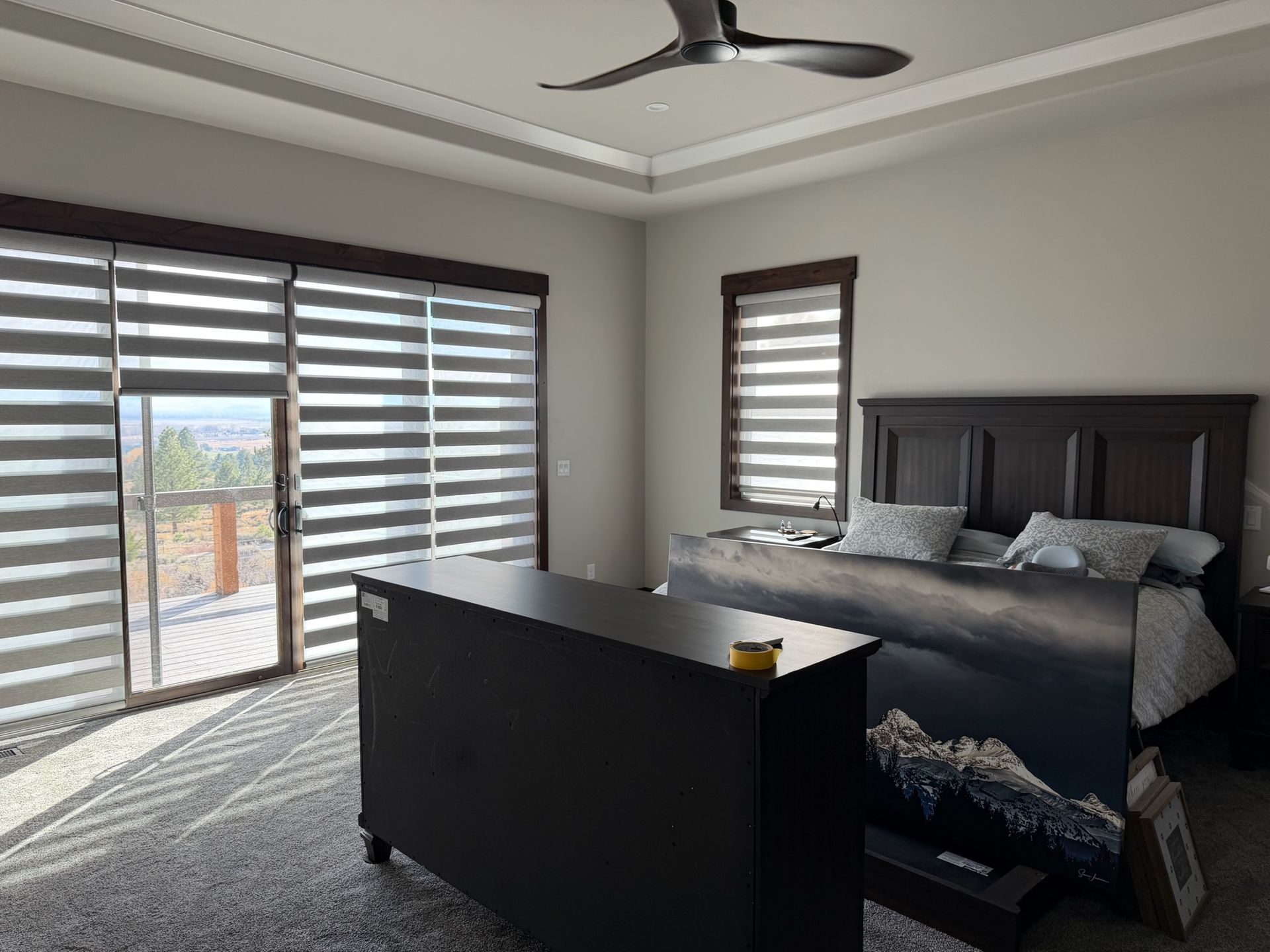 Modern bedroom with gray bed, black dresser, ceiling fan, and large striped window shades