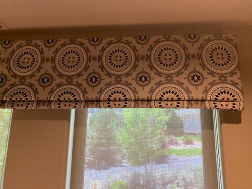 Patterned fabric window valance above a sunlit window with a mesh screen