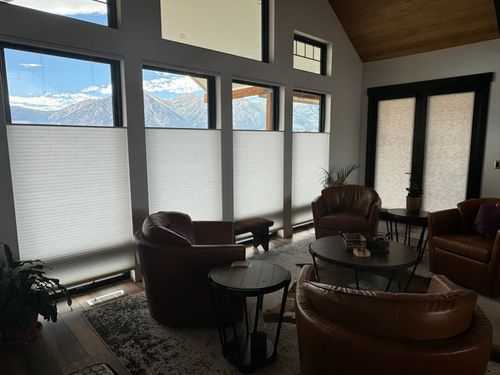 Modern living room with brown leather chairs, round tables, and large windows with mountain view.