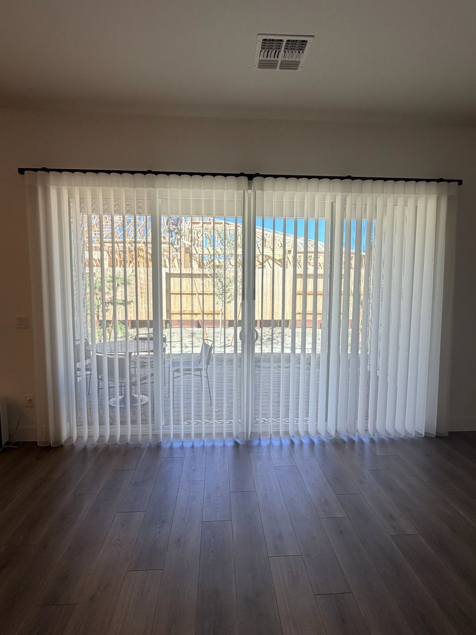 Empty living room with wood floors and large sliding glass doors covered by sheer curtains.