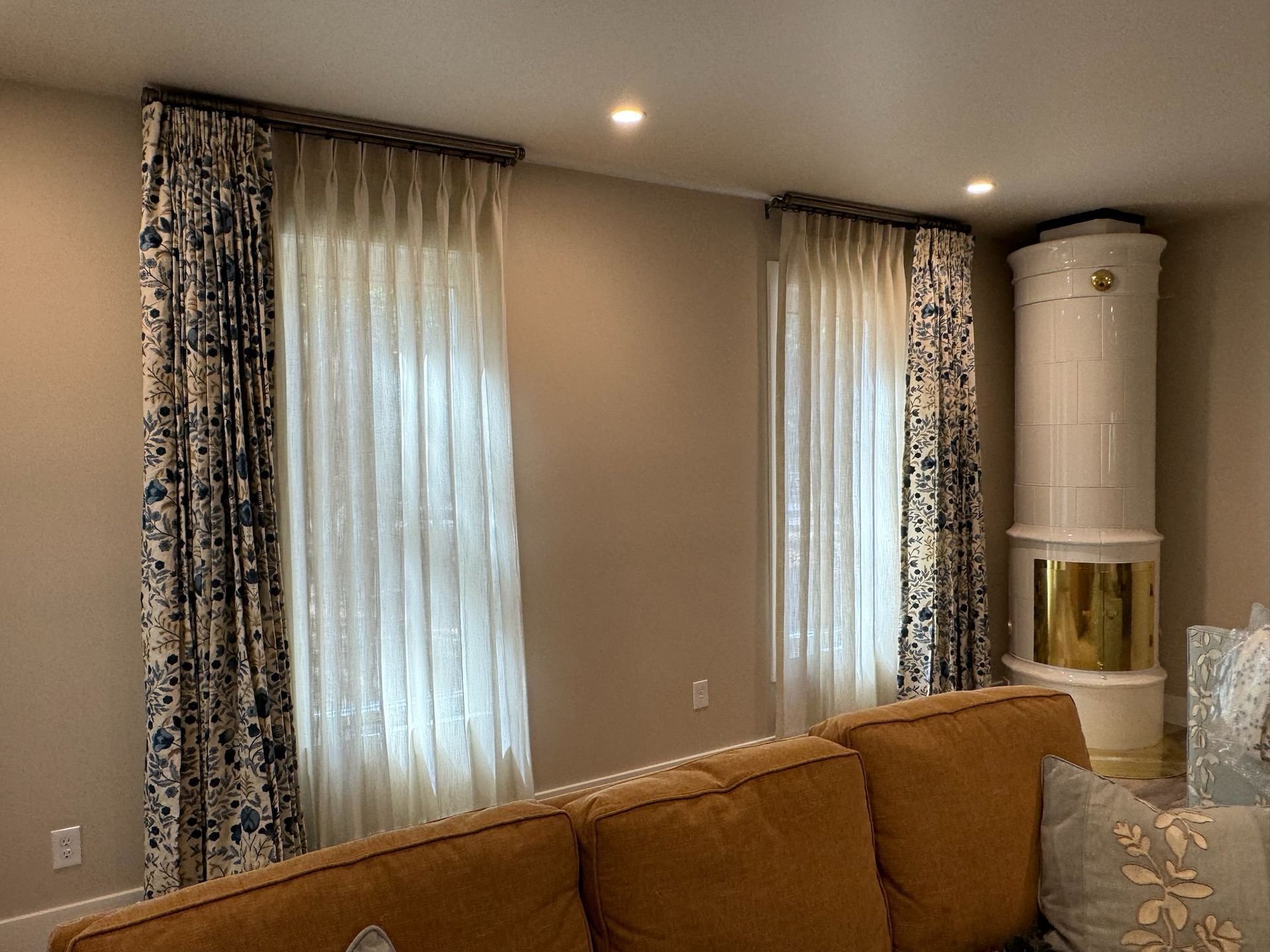 Cozy living room with beige walls, tall windows with curtains, and a brown sofa in the foreground