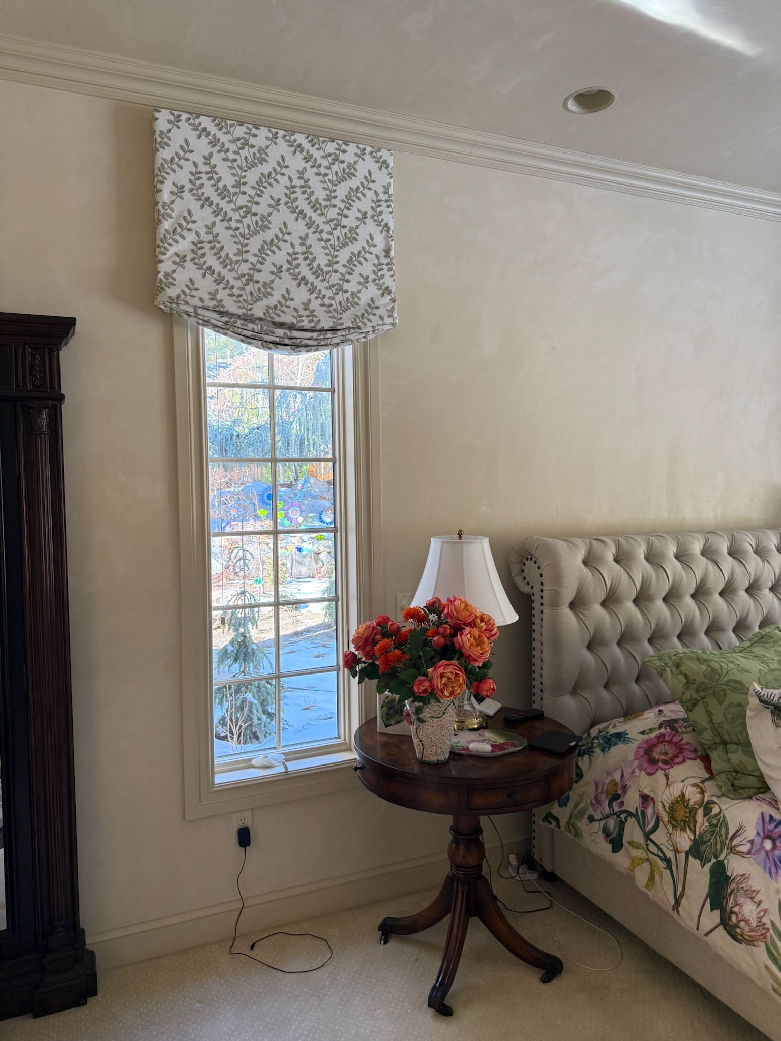Bedroom corner with floral window shade, bedside table lamp, and tufted upholstered headboard