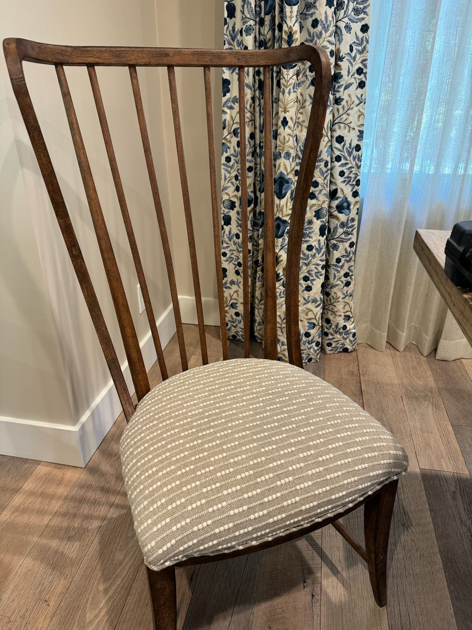 Wooden dining chair with beige upholstered seat beside curtains and a window indoors