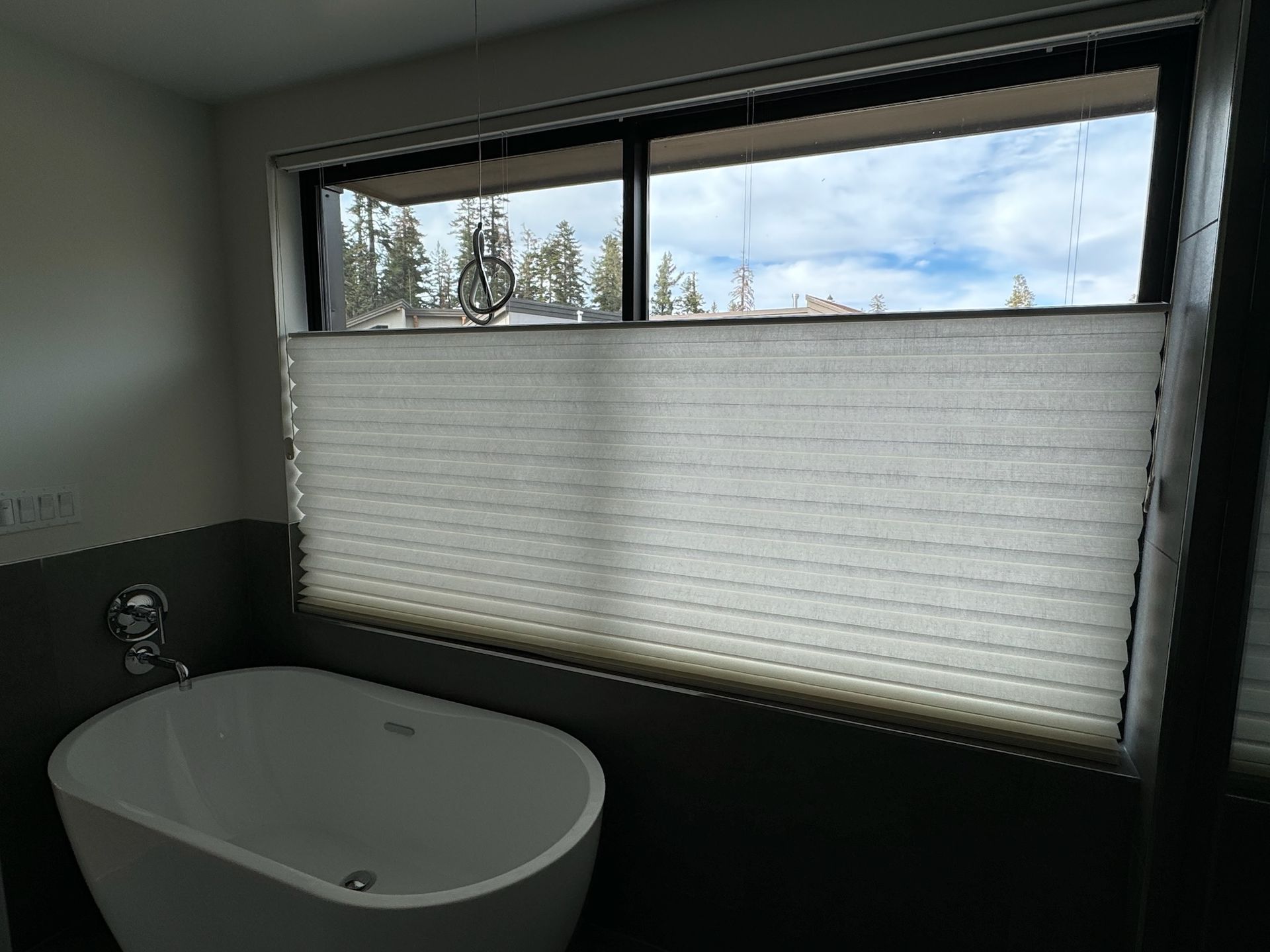 Bathroom with a freestanding tub beside a large frosted window showing trees outside