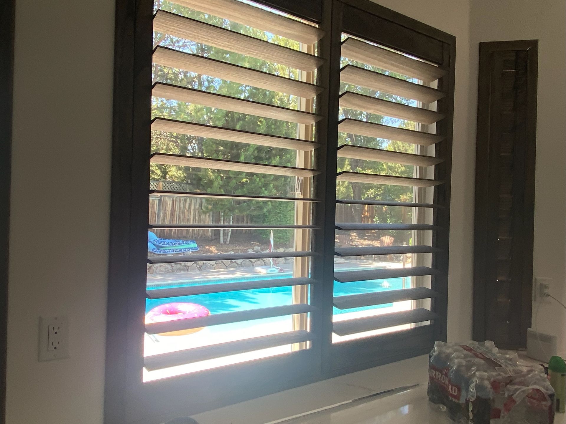 Living room window with slatted blinds overlooking a backyard pool and trees