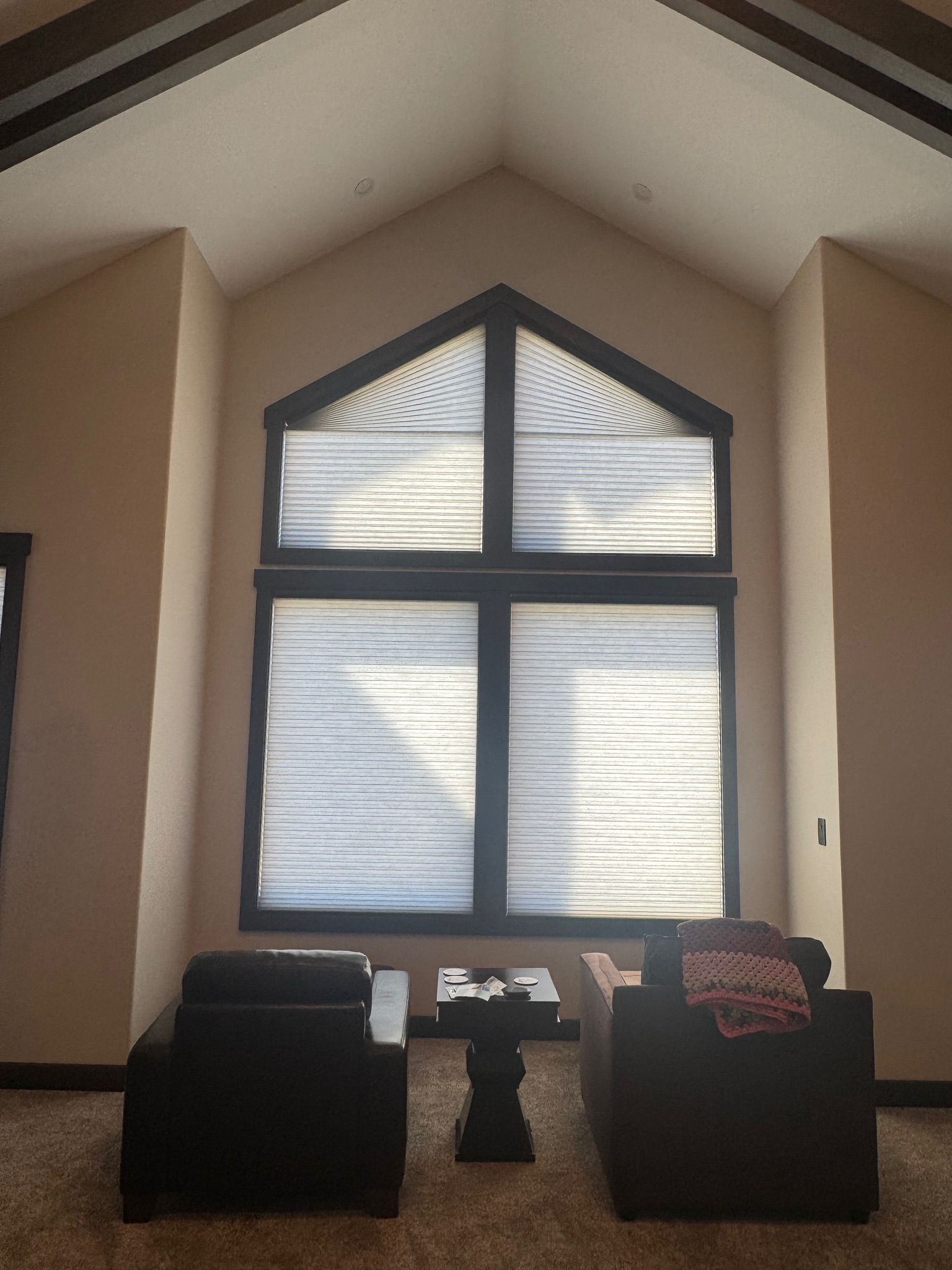 Living room with vaulted ceiling, arched window, and two black chairs facing a small table.
