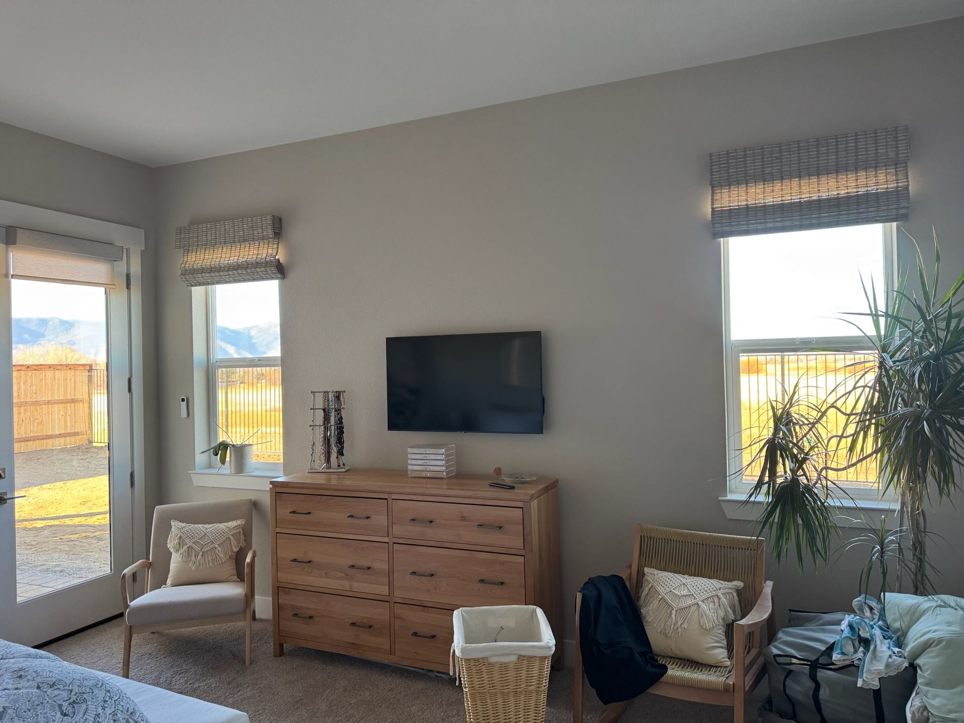 Bright living room with TV, wooden dresser, chairs, and two windows with curtains.