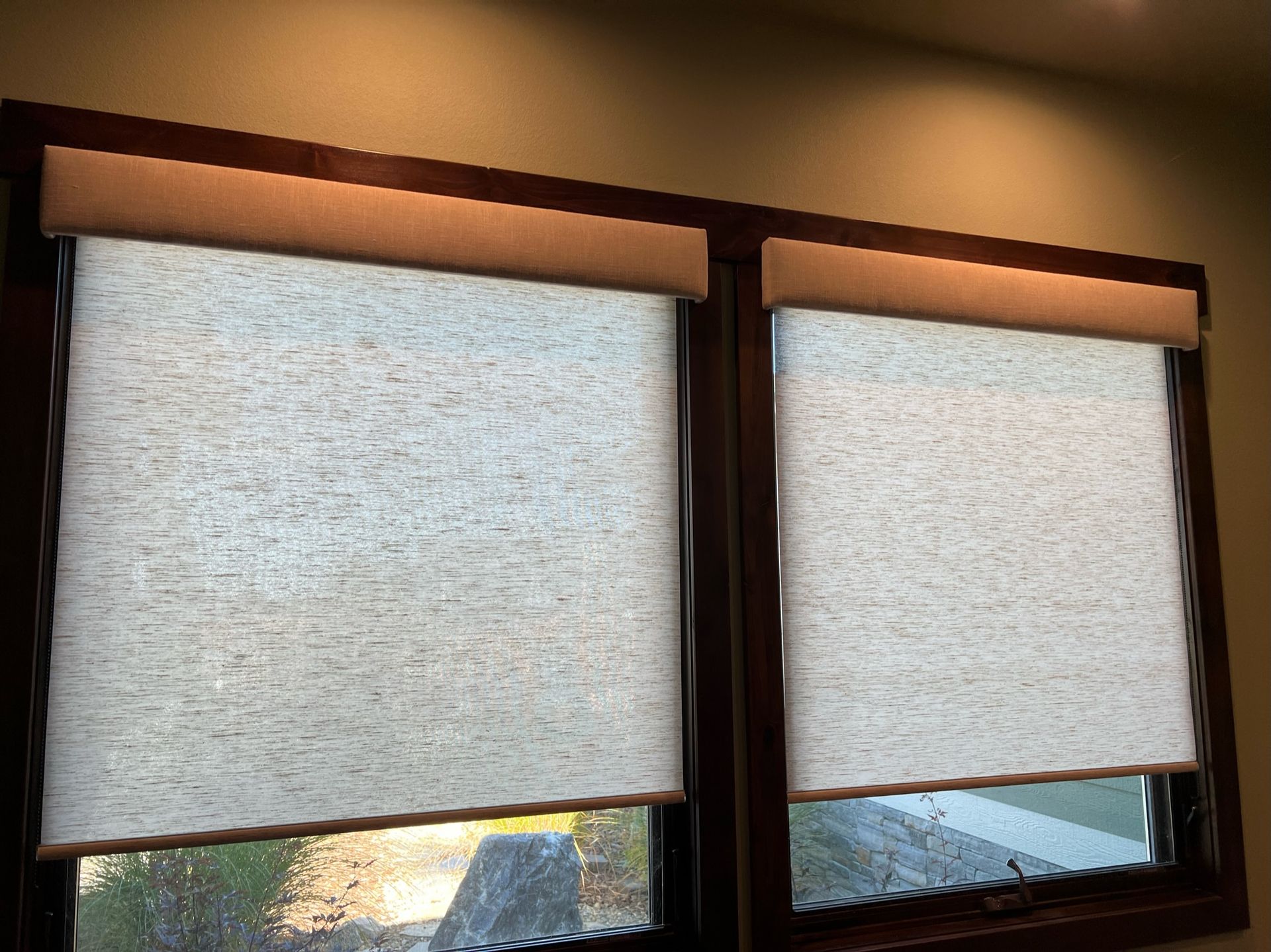Two closed white window shades on brown-framed windows in a room