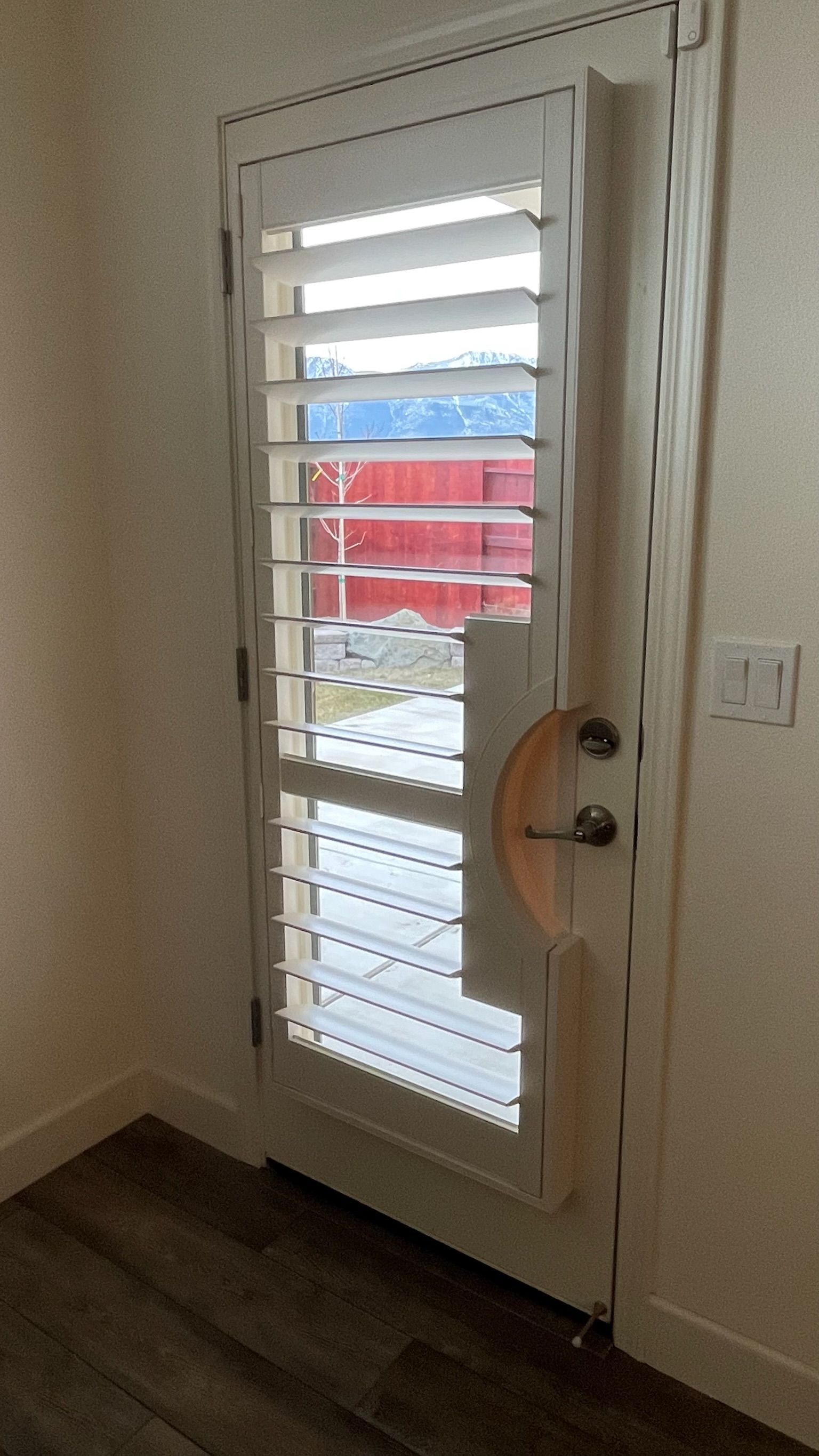 White door with glass blinds and view of a red vehicle outside, inside a room with beige walls.