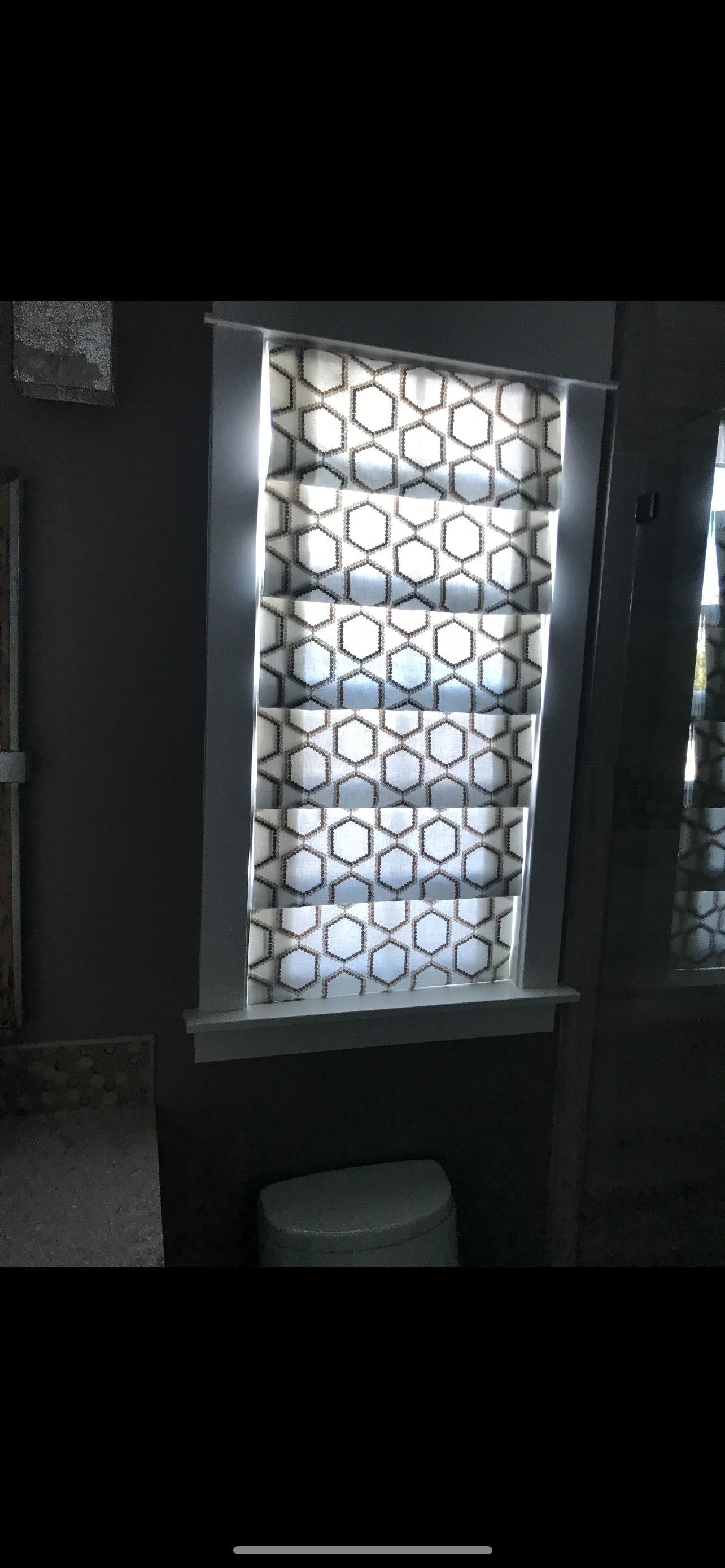 Dim room with a bright window covered by patterned sheer curtains, and a toilet visible below.