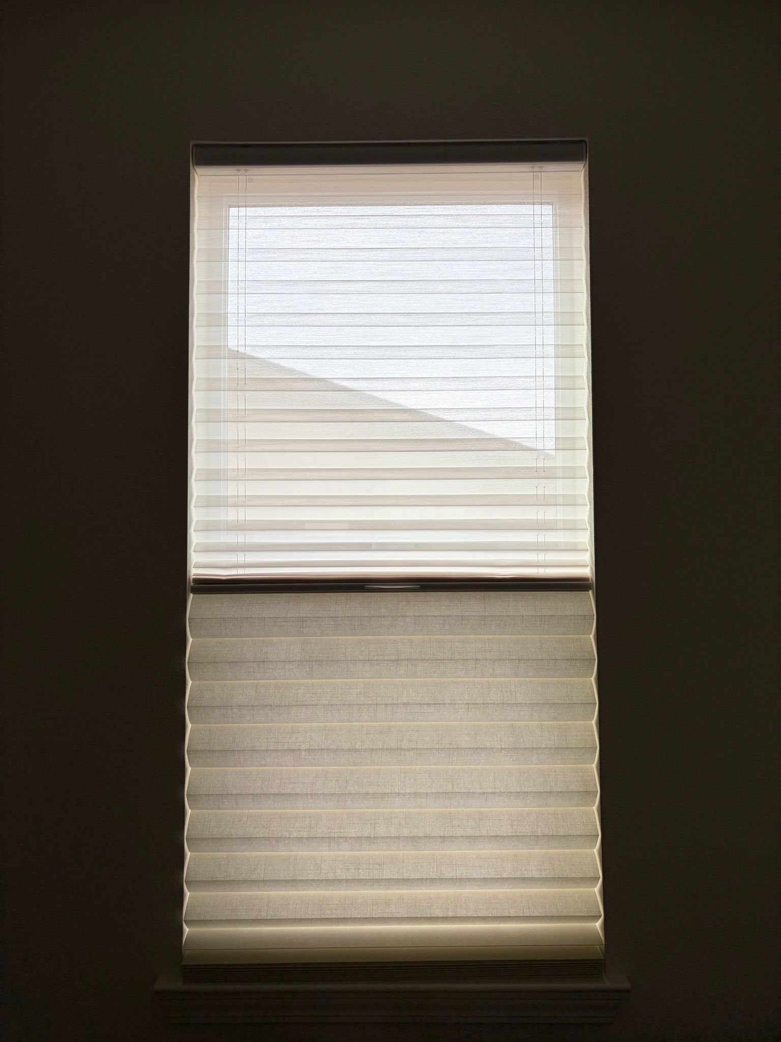Partially open window blinds with daylight showing through, one shade raised and one lowered