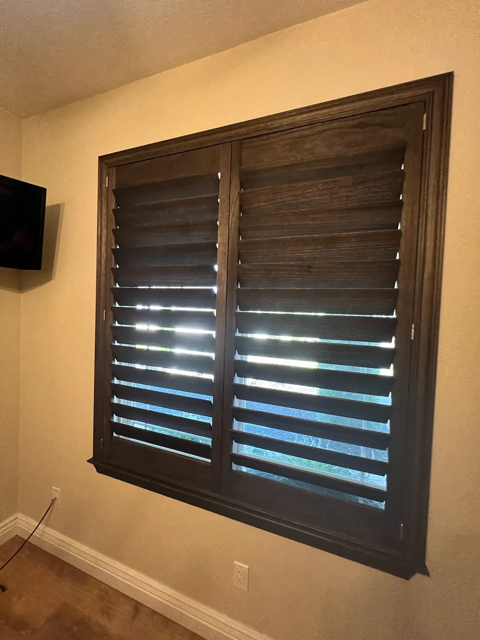 Brown window shutters with horizontal slats on a beige wall in a room with carpet and a wall-mounted TV