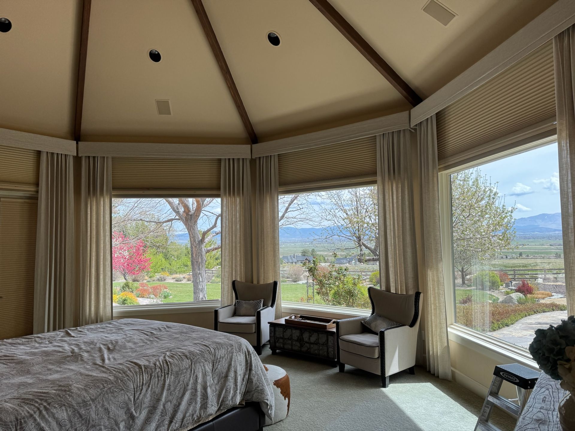 Luxurious bedroom with large bay windows overlooking mountains and a garden