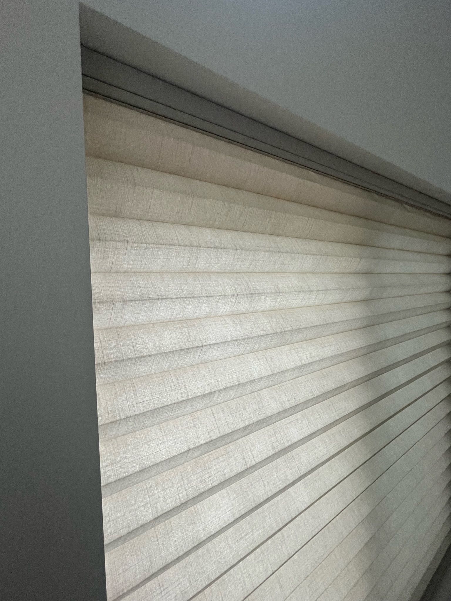 Closed white window blind beside a gray wall, softly lit by daylight