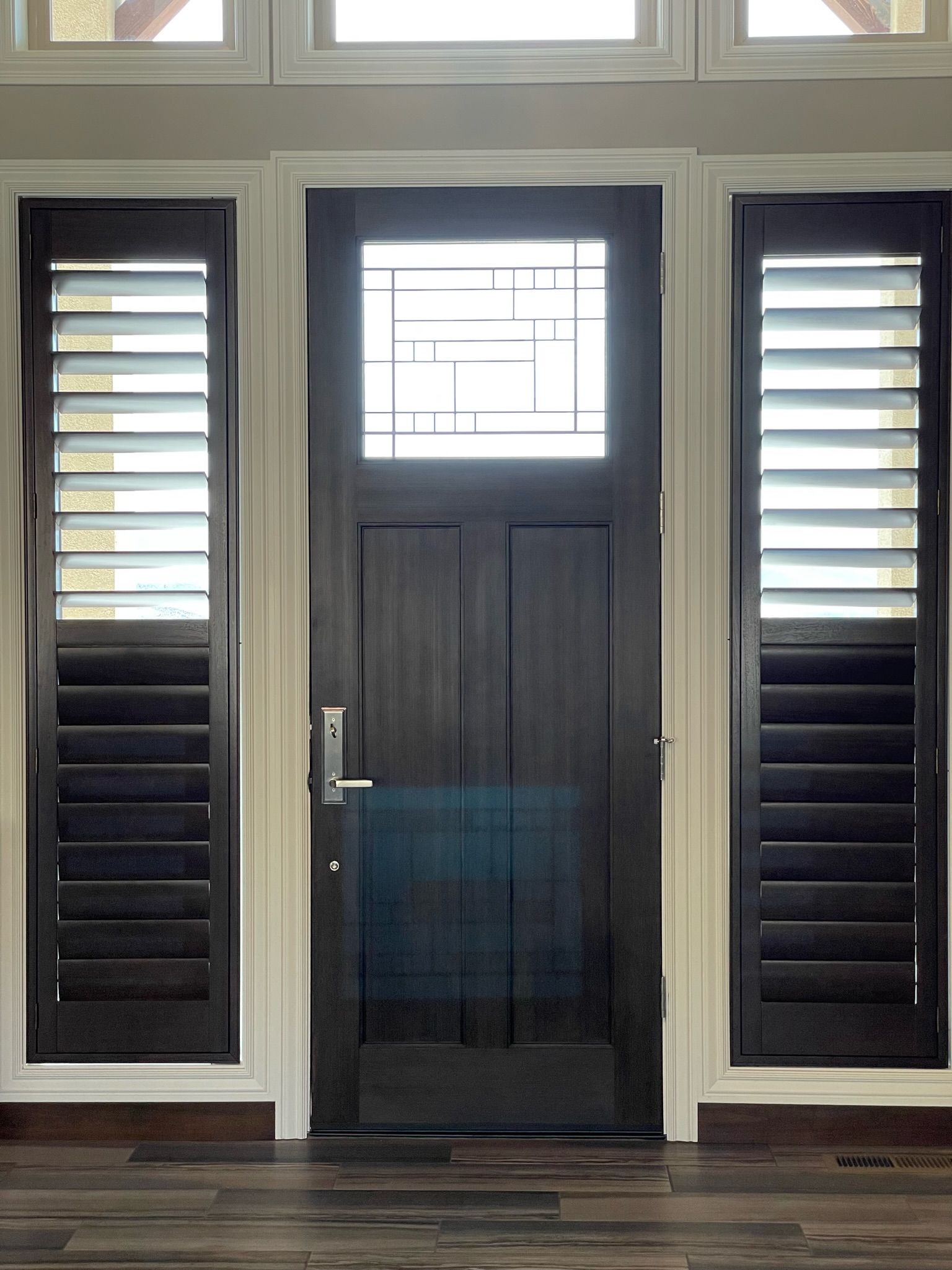 Front door with sidelights and a small window, framed by dark shutters and white trim.