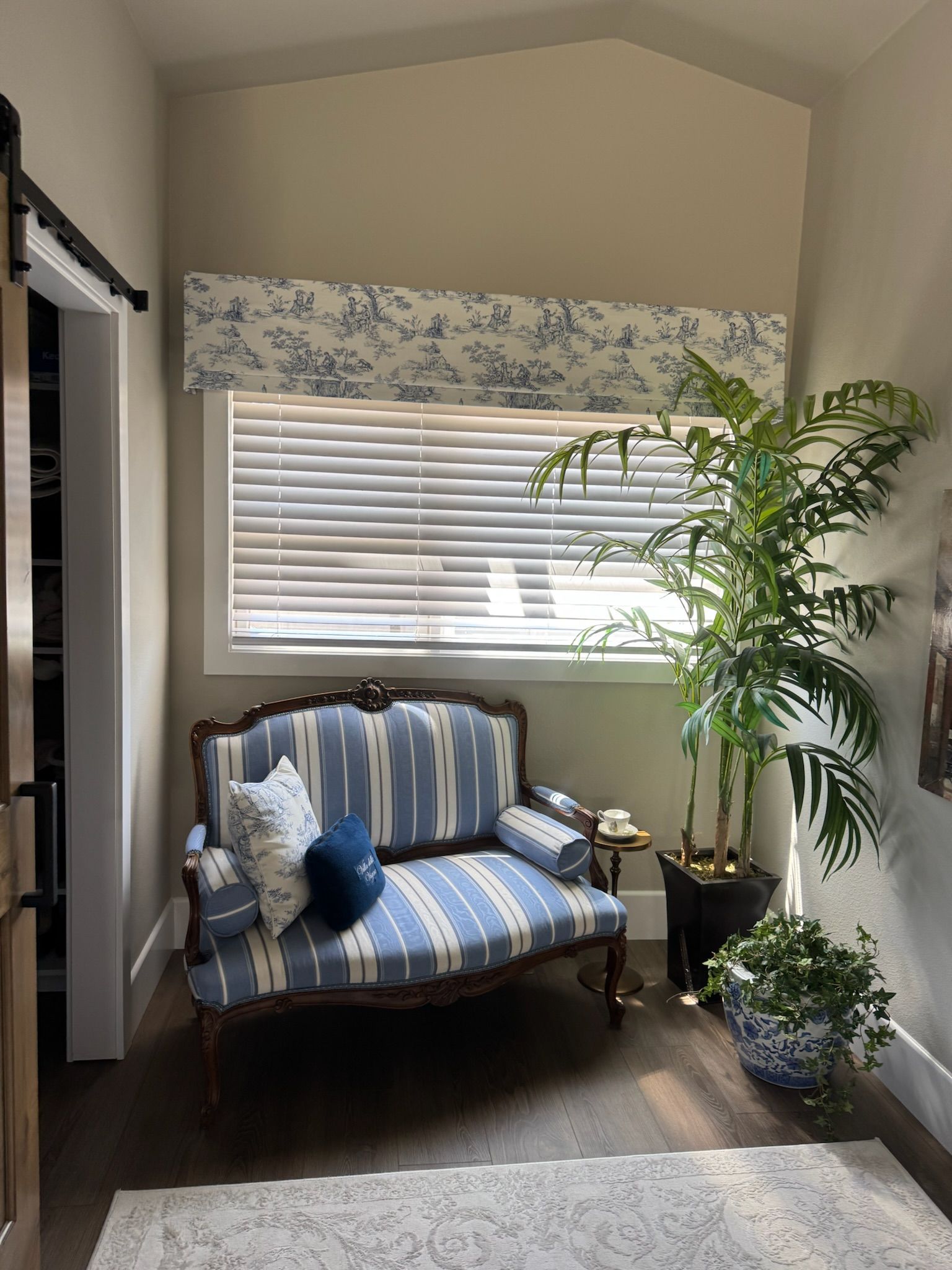 Cozy corner with striped armchair, window blinds, floral valance, and potted plants in a bright room