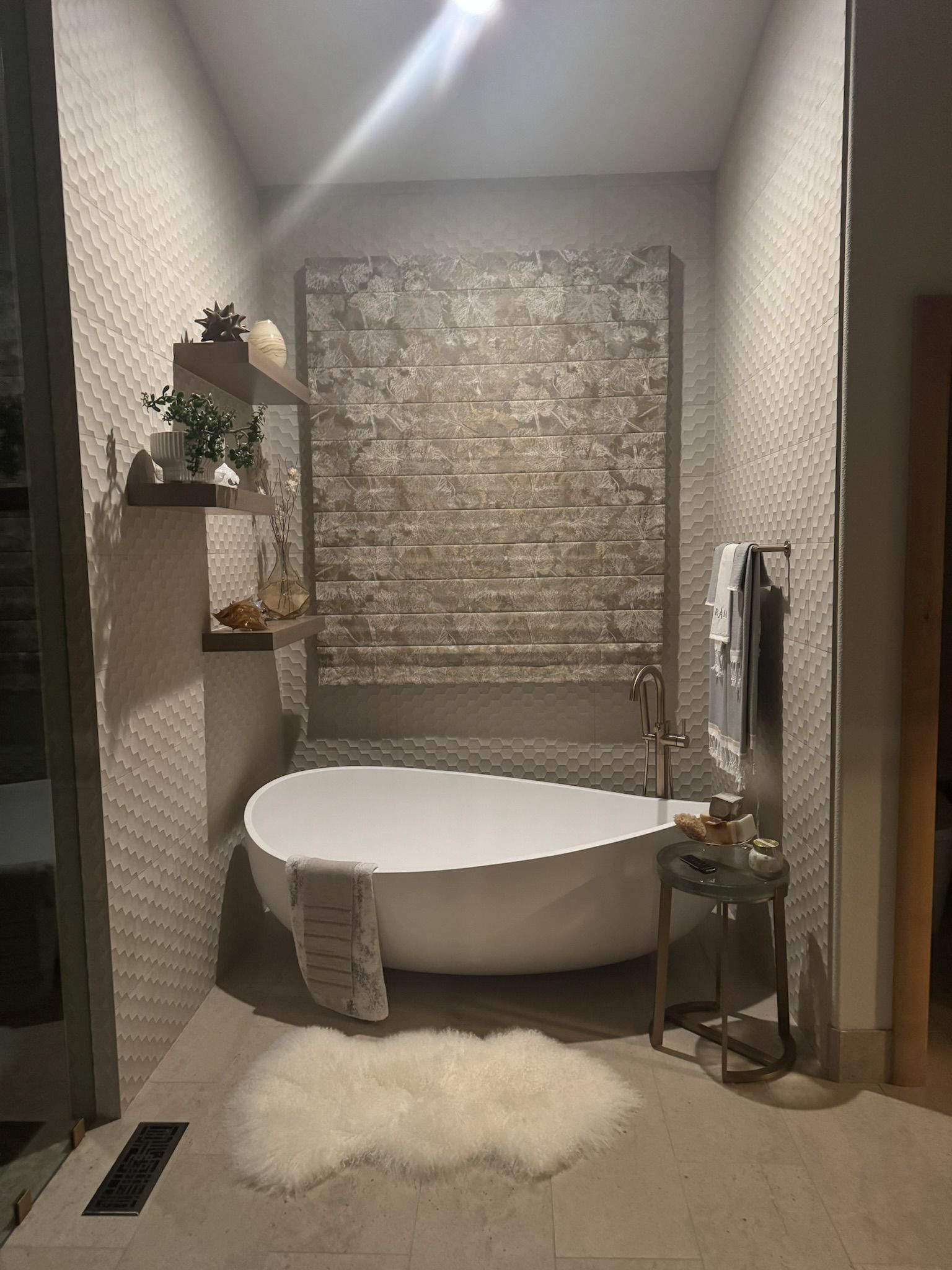 Small bathroom with freestanding white tub, stone accent wall, wall shelves, and fluffy white rug