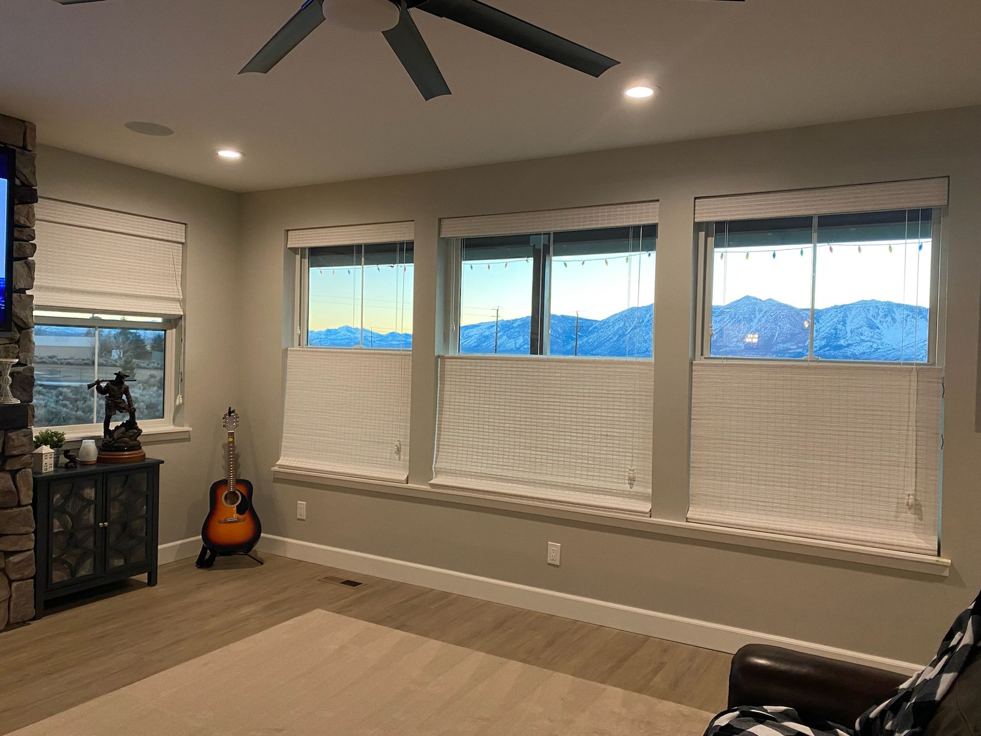 Empty living room with beige walls, large windows, a guitar by the wall, and mountains visible outside.