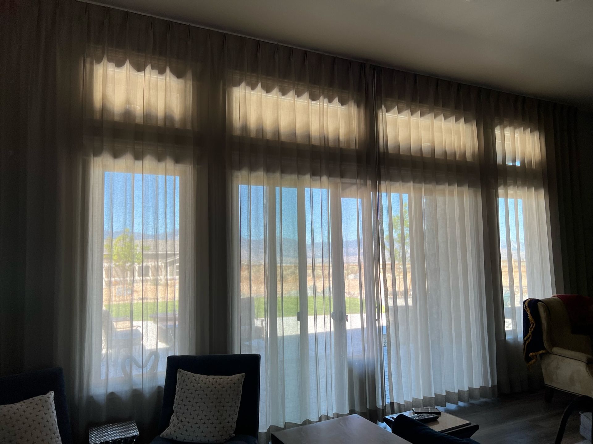 Sheer curtains over large windows with sunlight and a dark chair in a living room