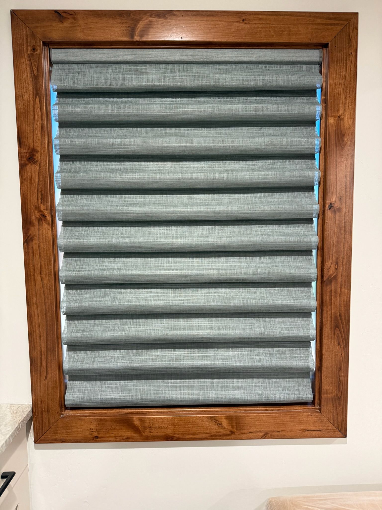 Wood-framed window with closed gray pleated blinds