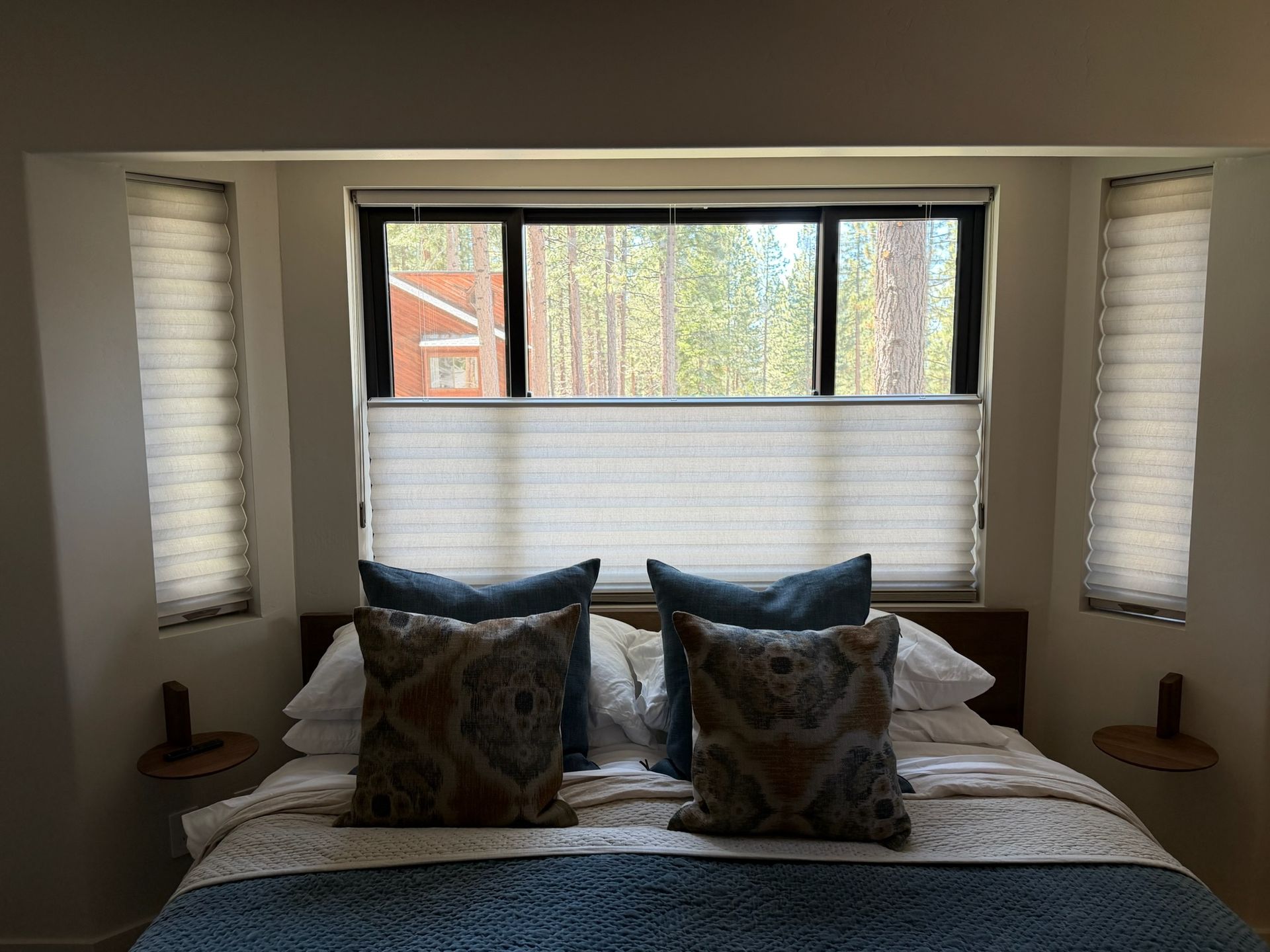 Bedroom with a neatly made bed, patterned pillows, and windows with blinds on three sides
