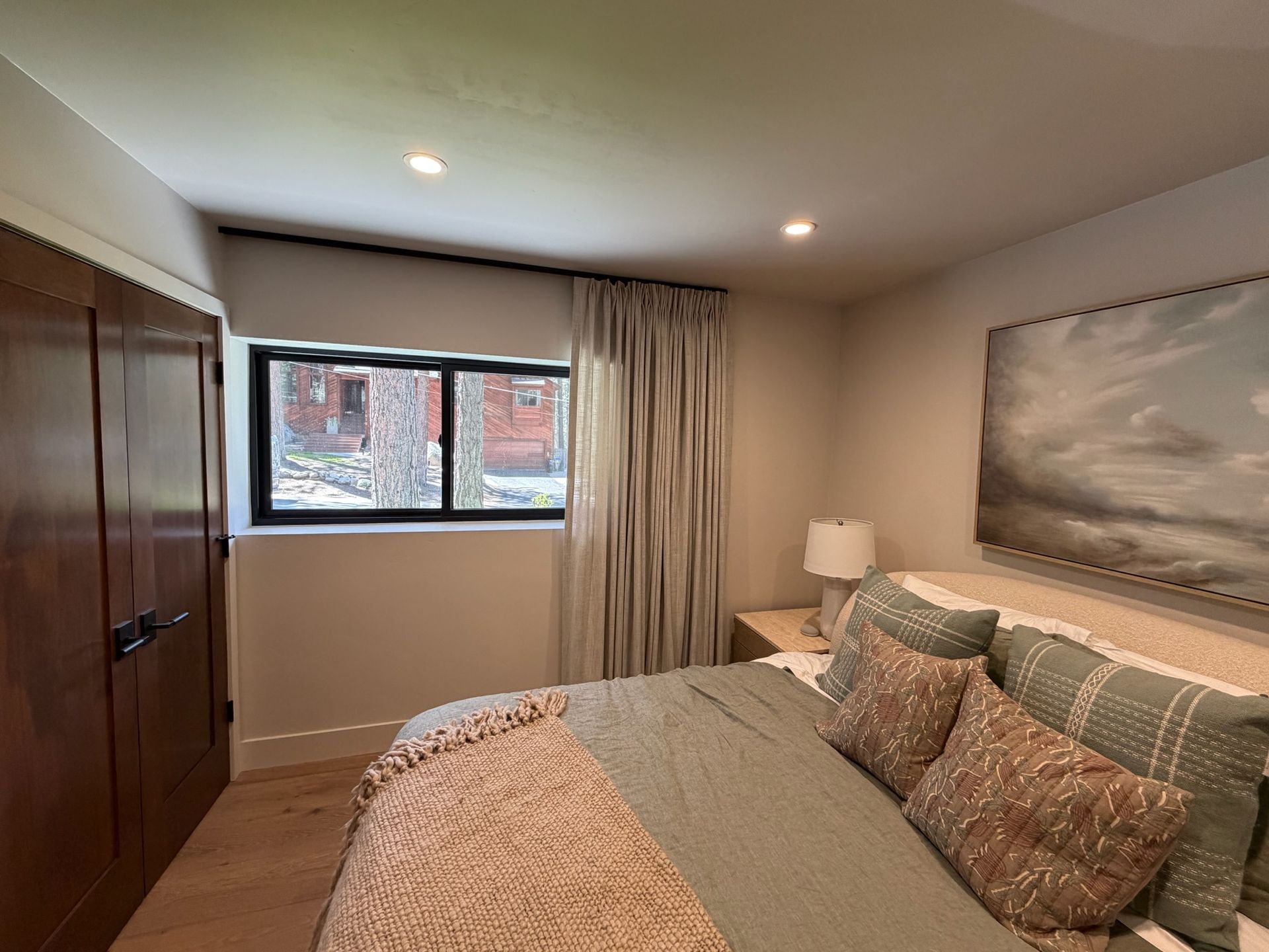 Bedroom with bed, wood wardrobe, window, and beige curtains in a neutral-toned room