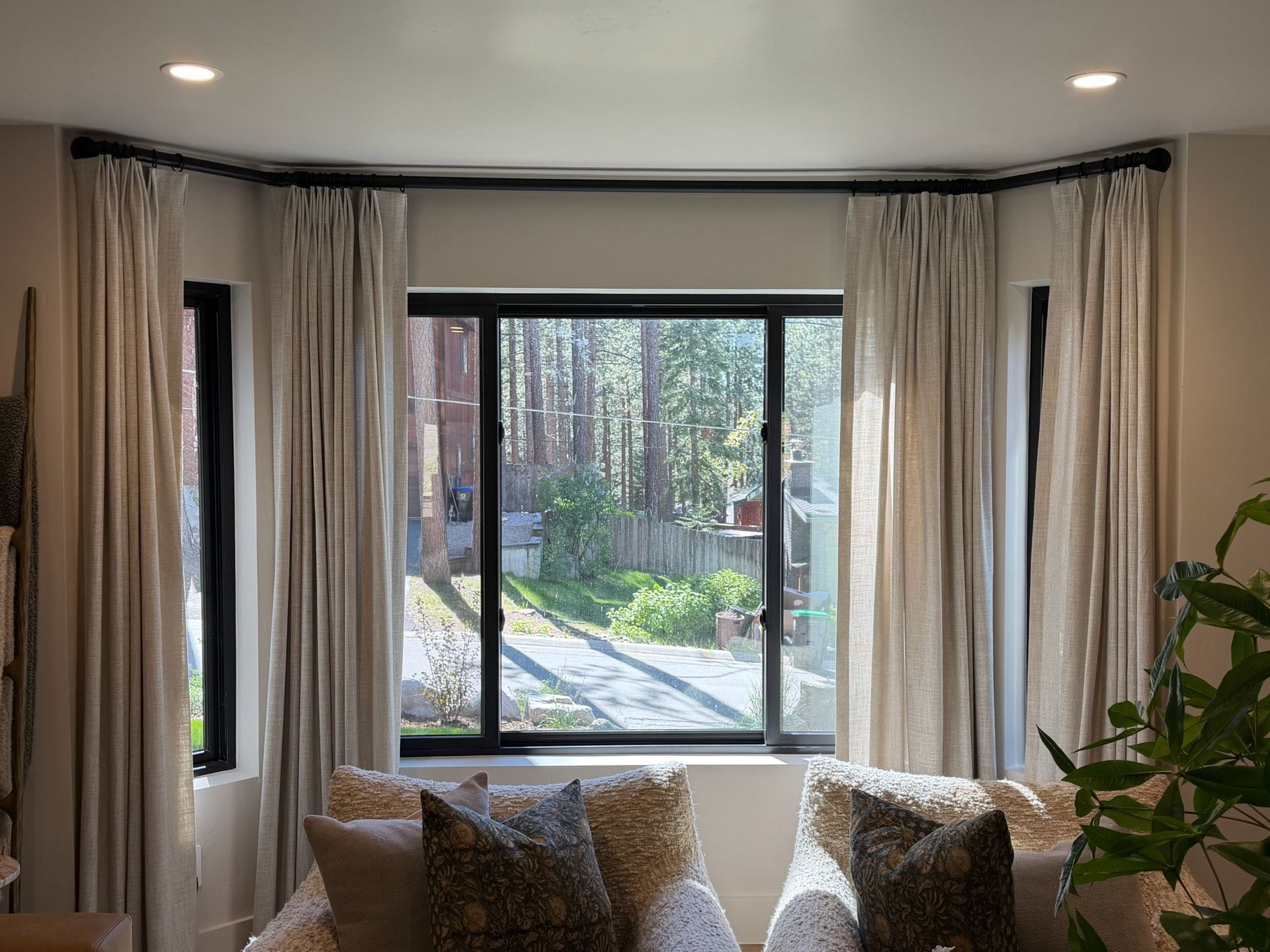 Living room with tall curtains, sofa, and large windows overlooking a tree-lined courtyard