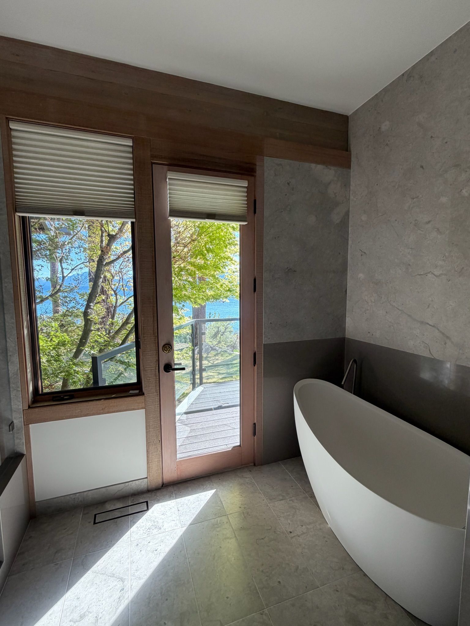 Modern bathroom with a white freestanding tub, glass door, and a view of trees outside.