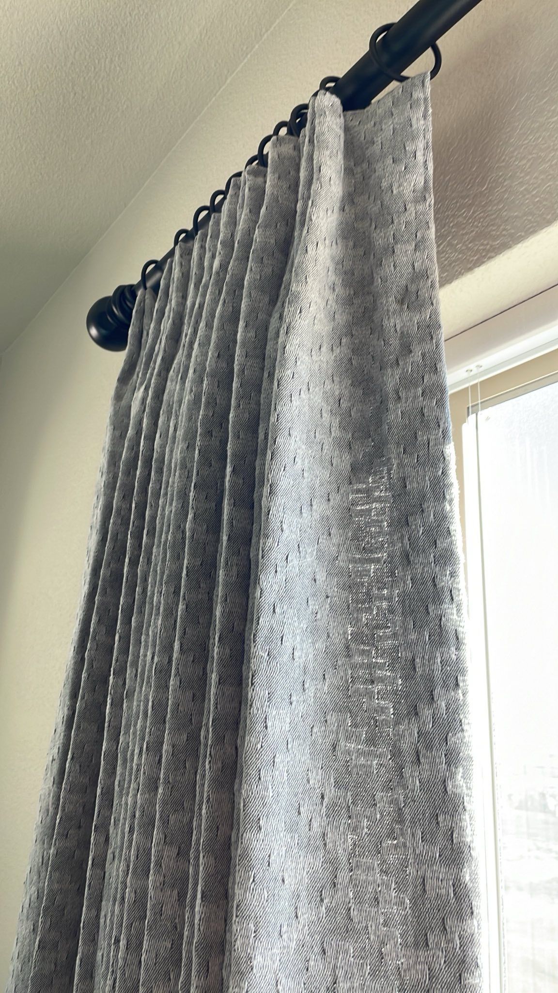 Gray curtain hanging from a black rod beside a bright window.