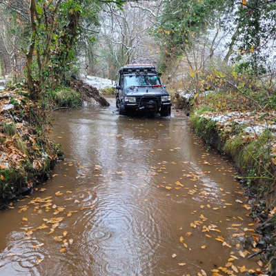 a black 4X4 is stuck in a muddy field with a winch attached to it .