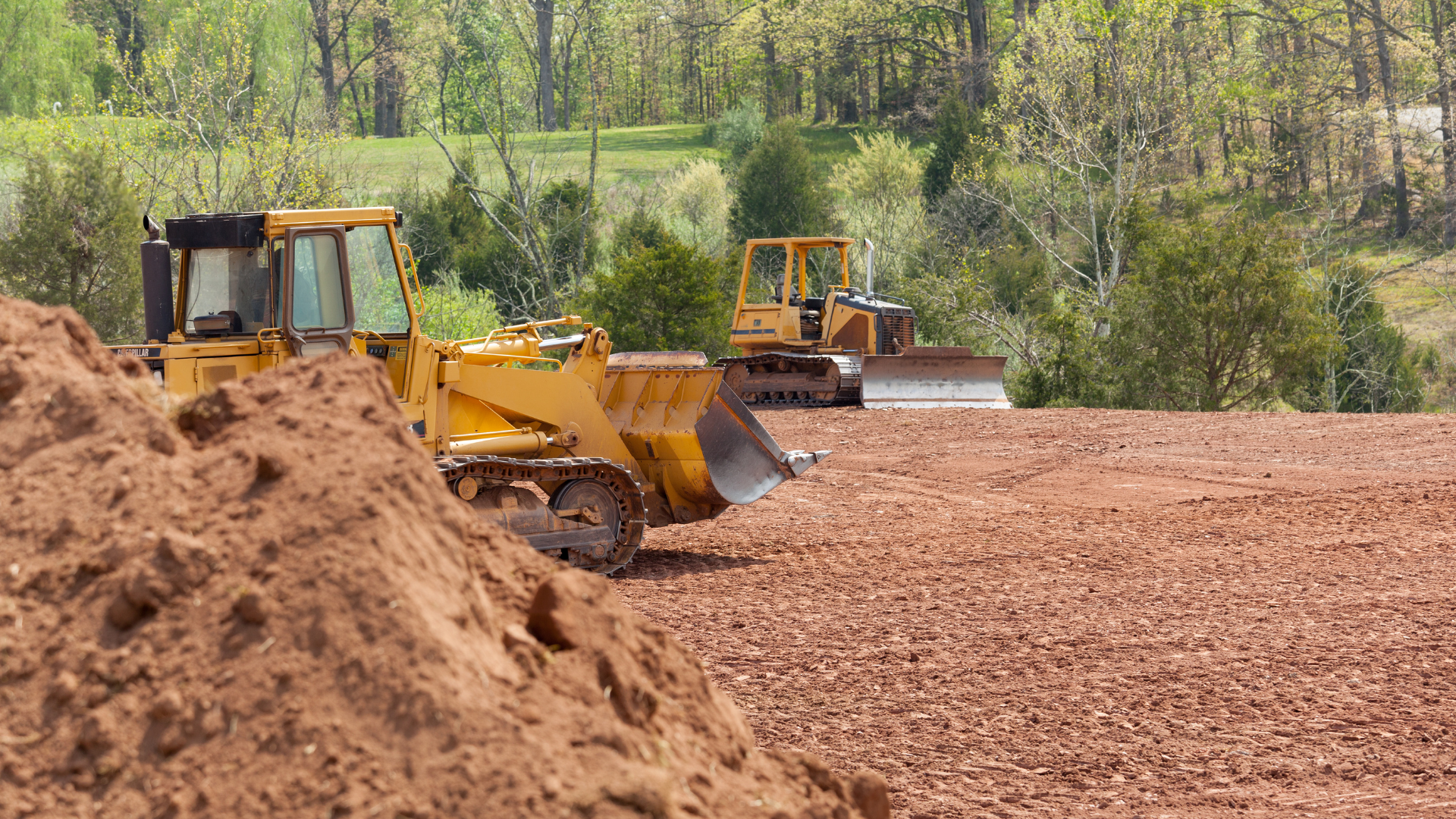 Two bulldozers are working in a dirt field.