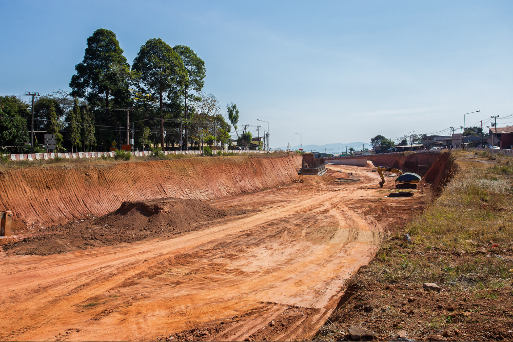 A dirt road is being built in a field with trees in the background.