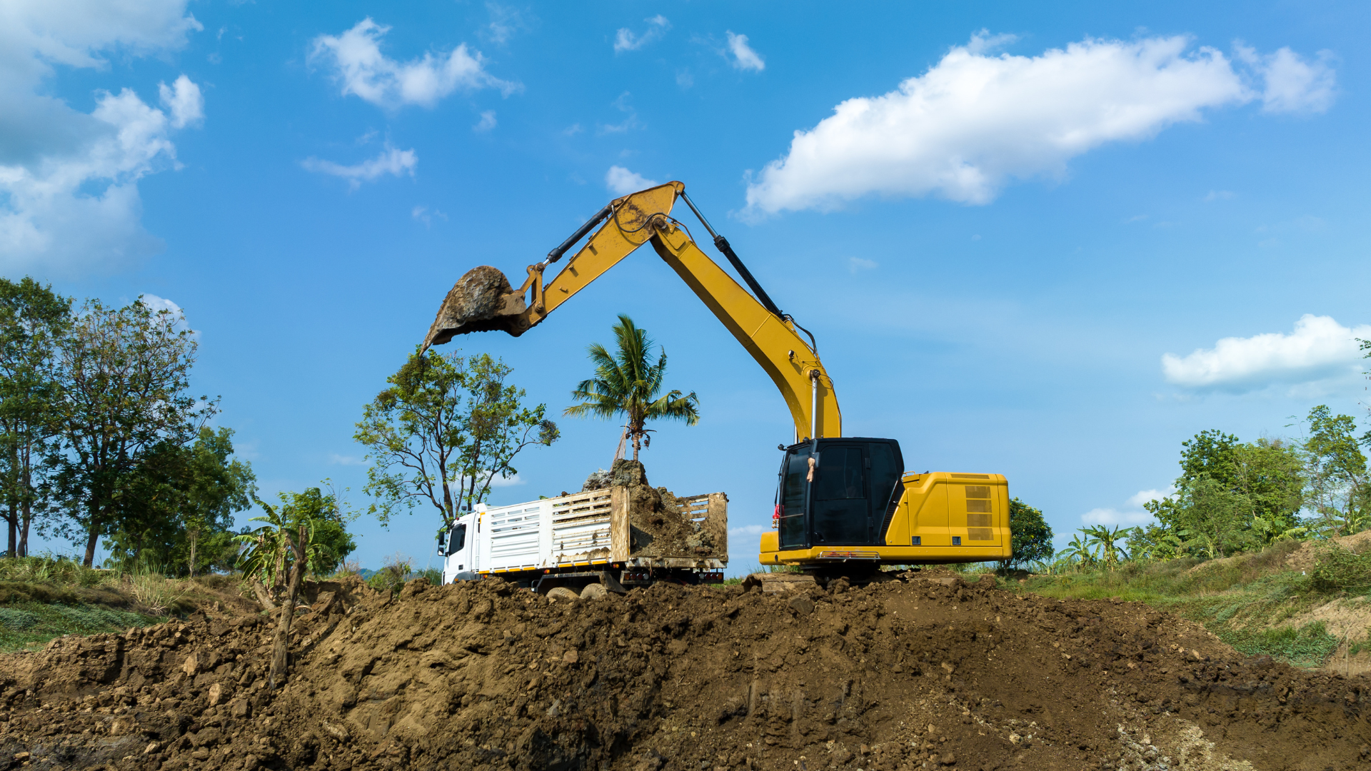 A yellow excavator is digging a hole in the dirt next to a truck.