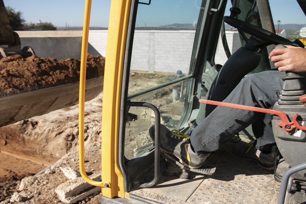 A man is driving a yellow excavator on a dirt road